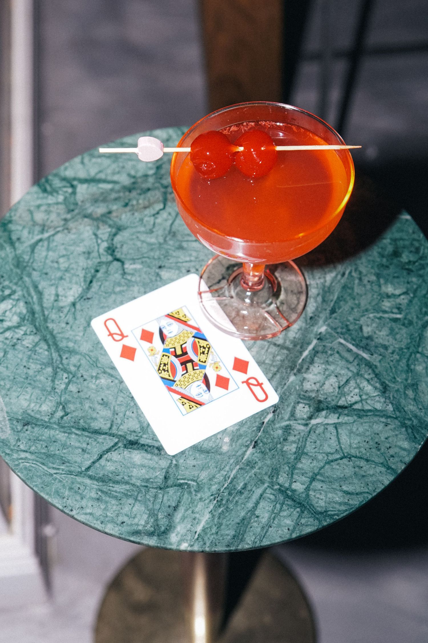 Orange cocktail and playing cards on green marble table.