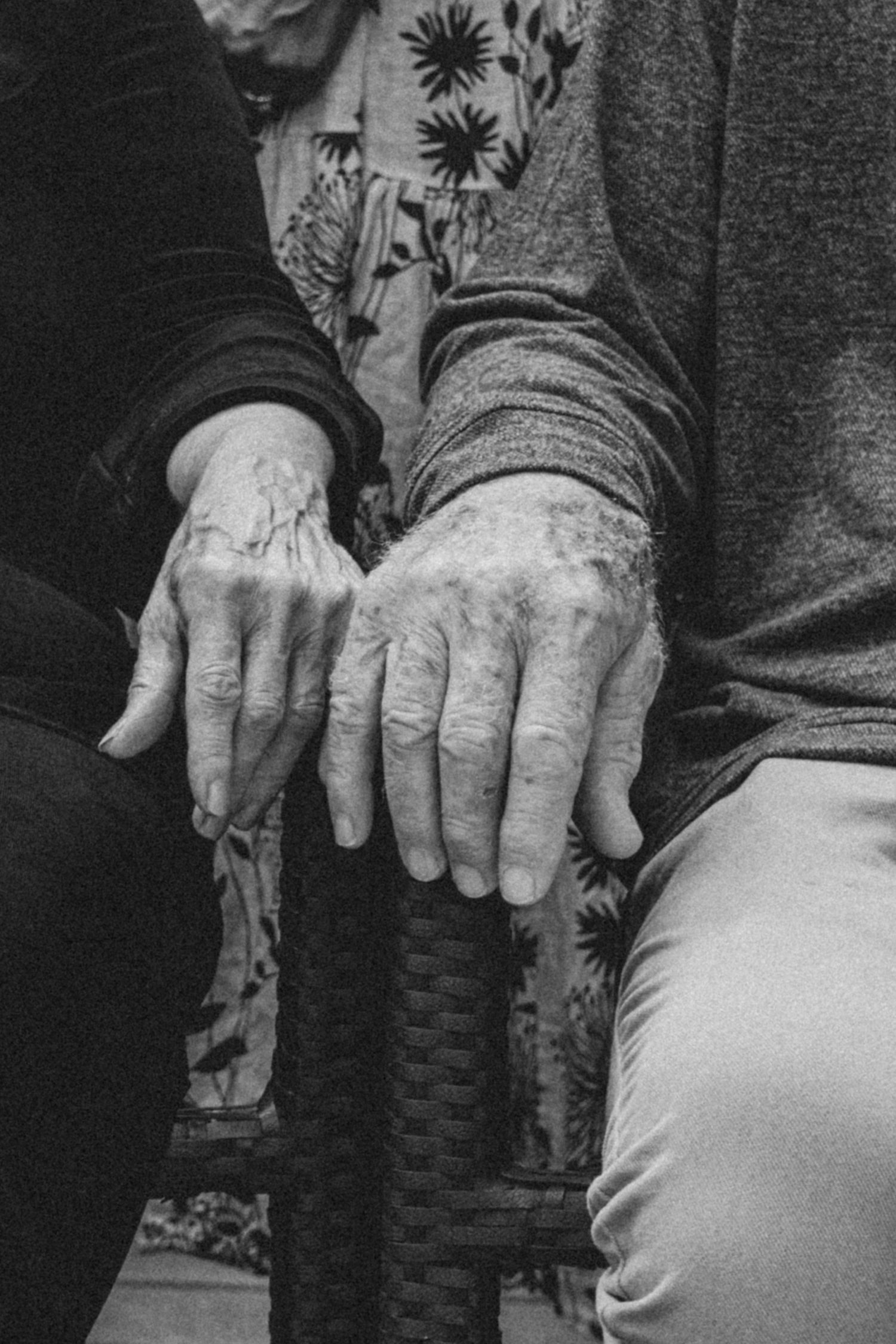 Close-up black and white photo of weathered hands resting on a woven surface.