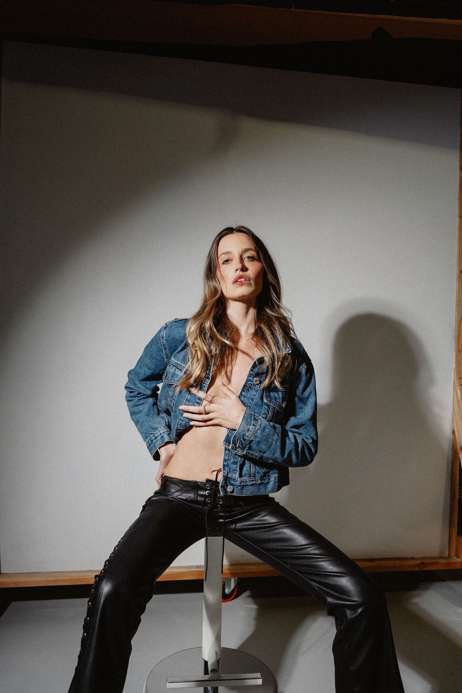 Studio fashion shoot featuring denim and leather outfit on metal stool.