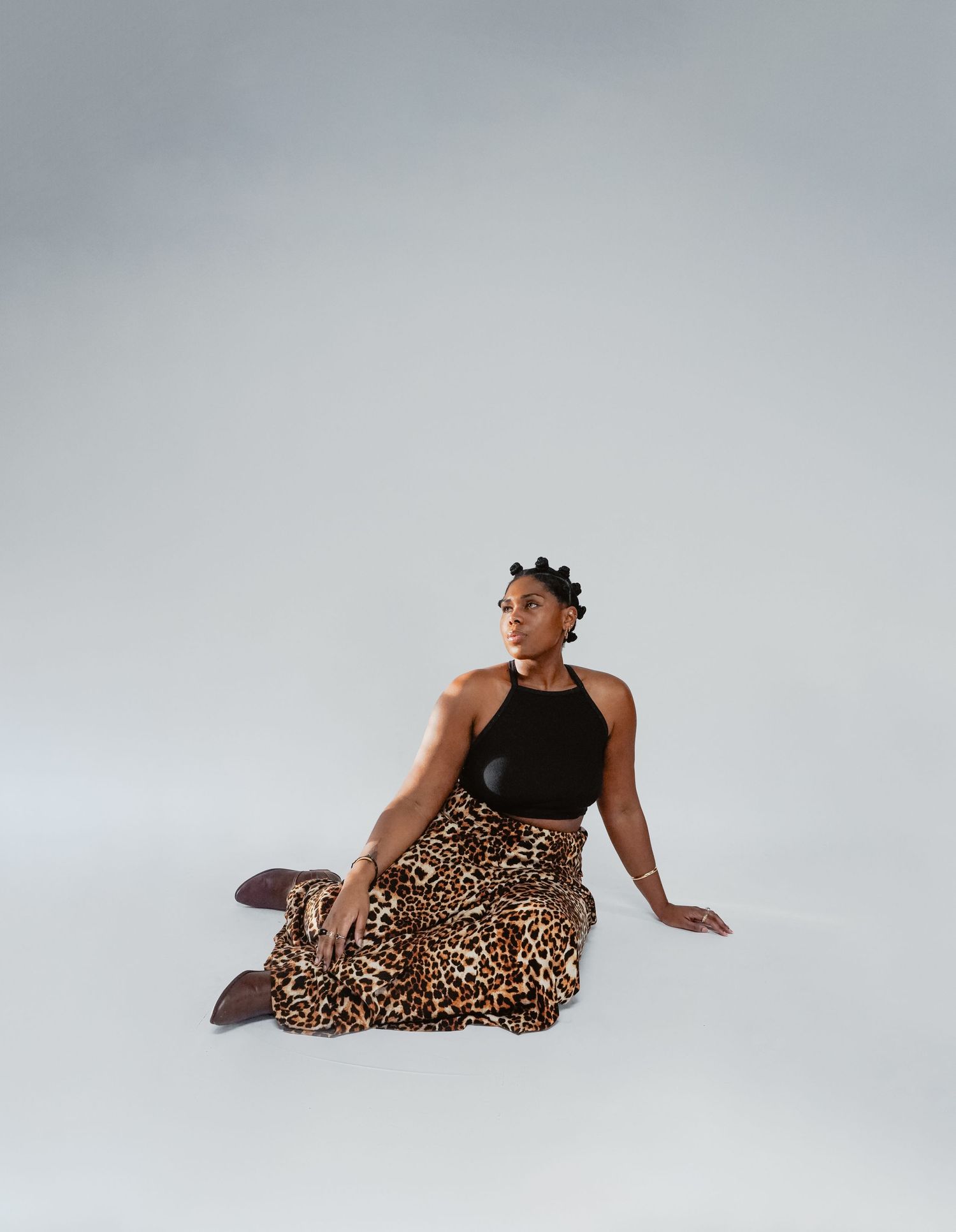 Fashion photo of model in black tank top and leopard print skirt against light gray backdrop.