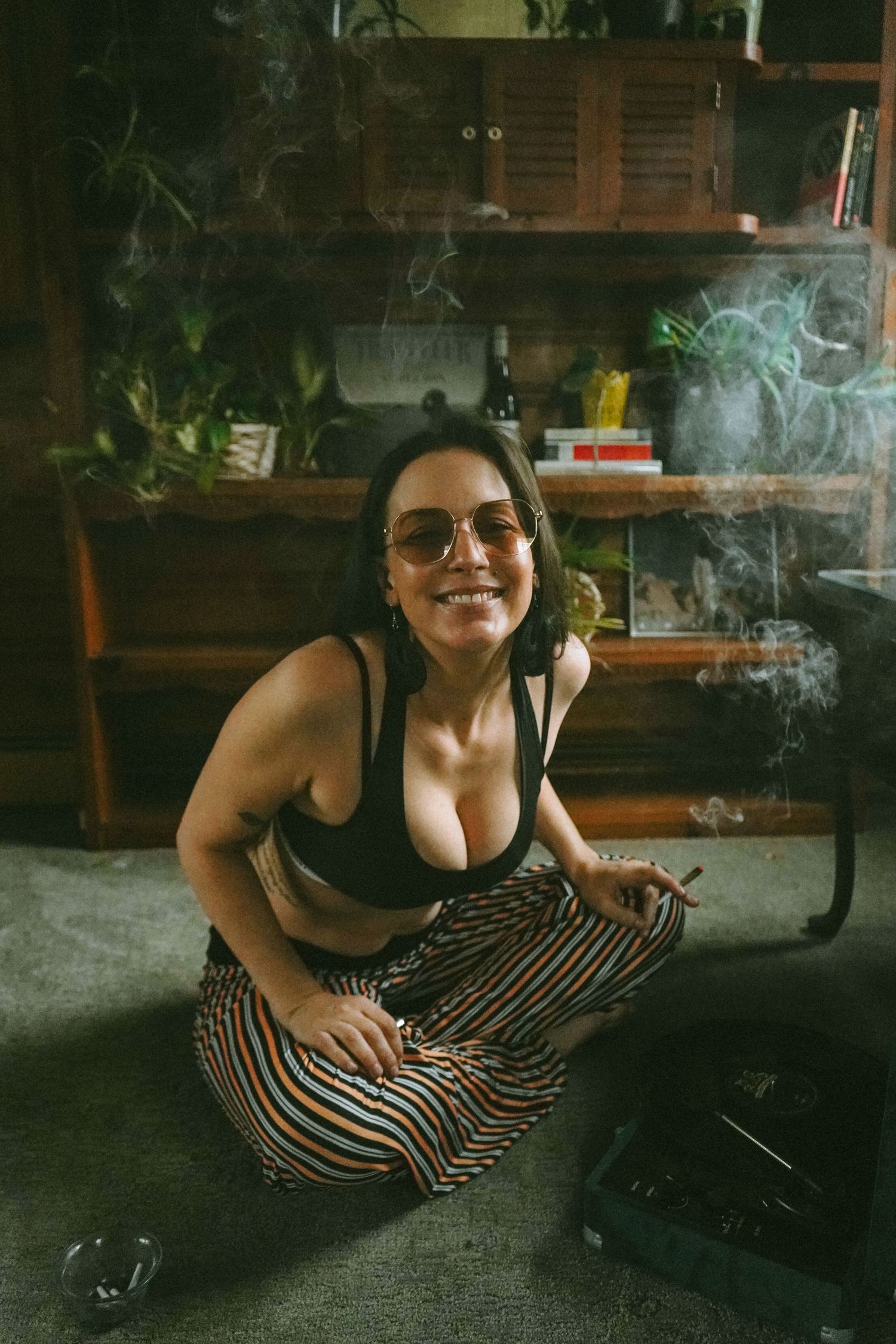 Person in striped pants sits on floor with record player and bookshelves.