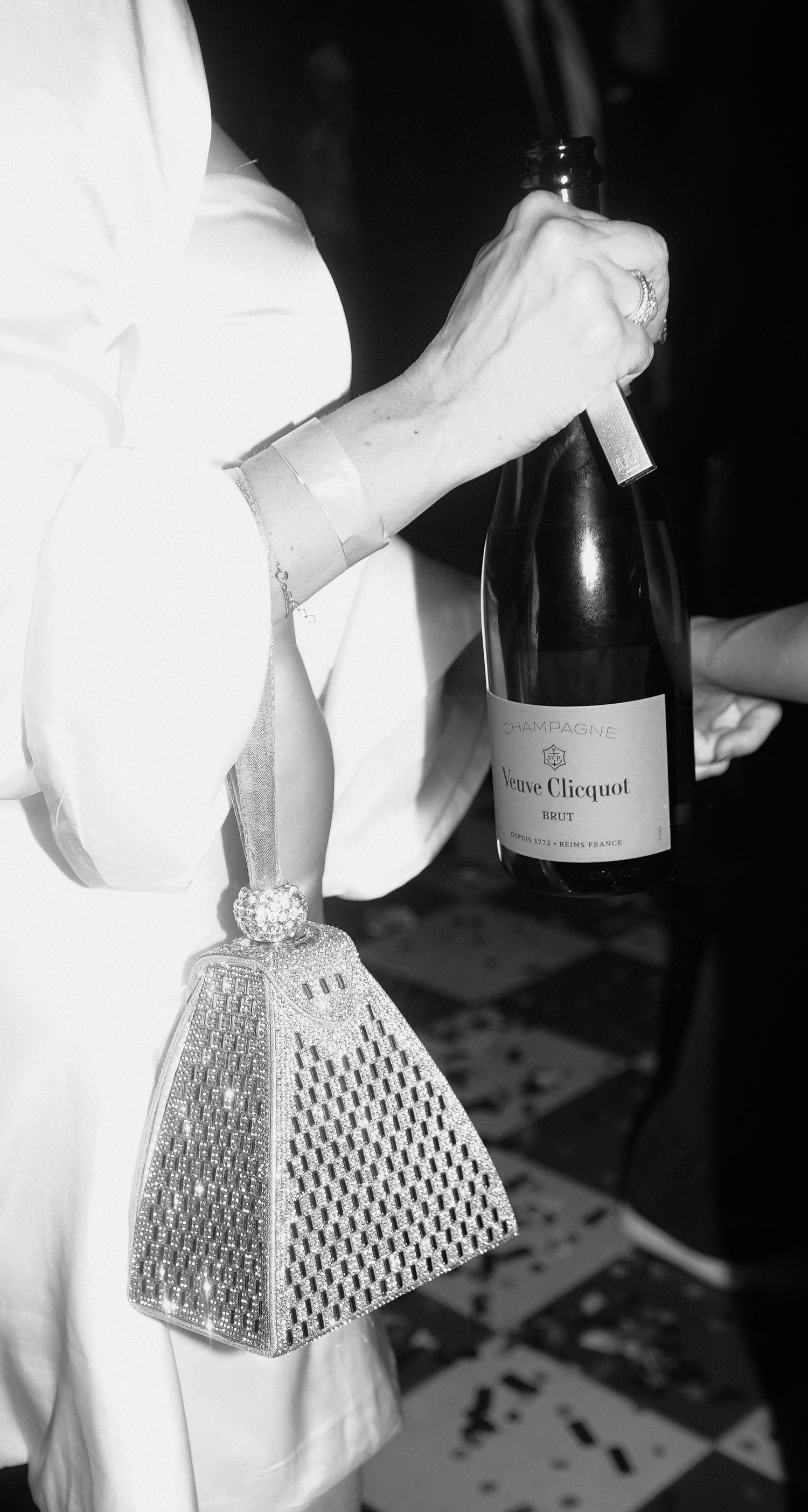 Black and white photo of someone holding a Veuve Clicquot champagne bottle with a sparkly purse.
