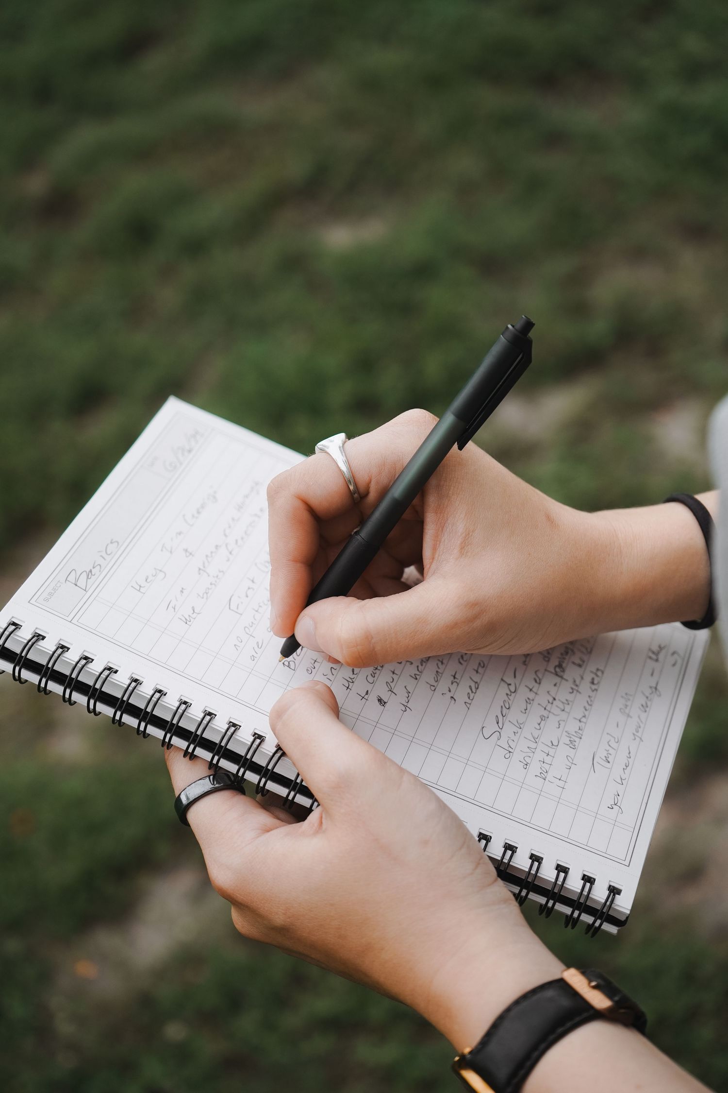 Close-up of hands writing in spiral notebook with black pen.