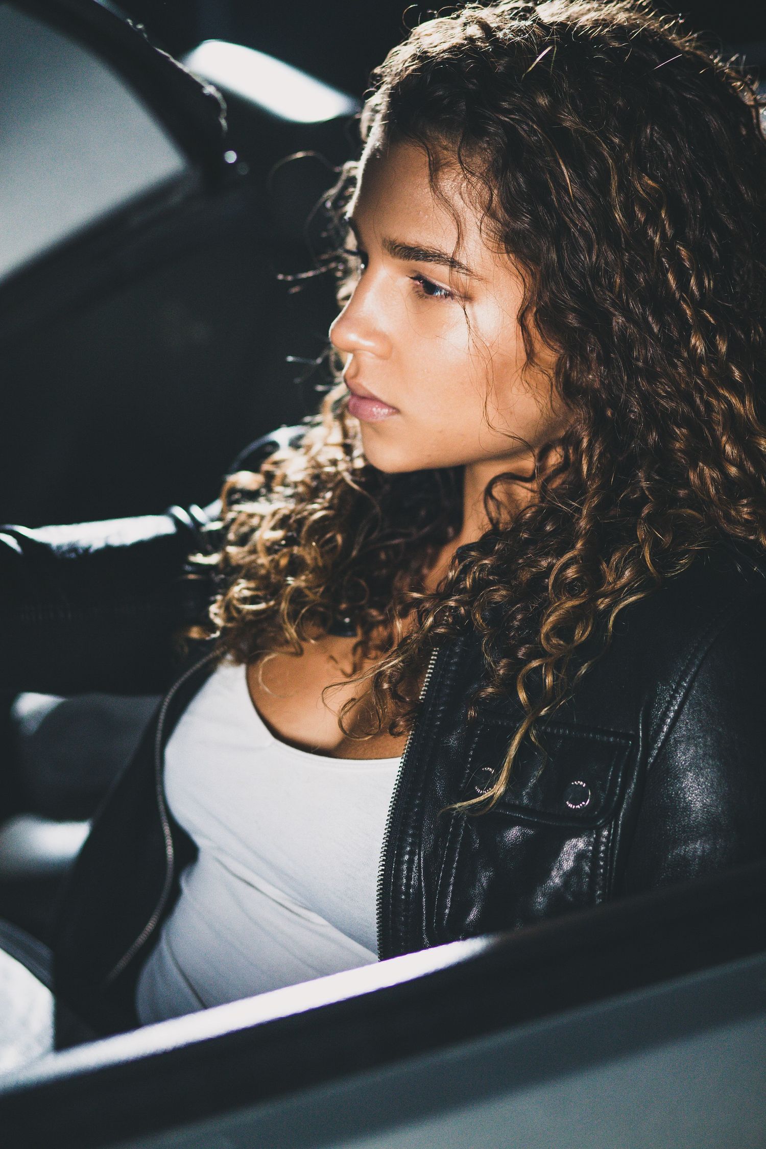 Side view of person with curly hair wearing leather jacket in car.