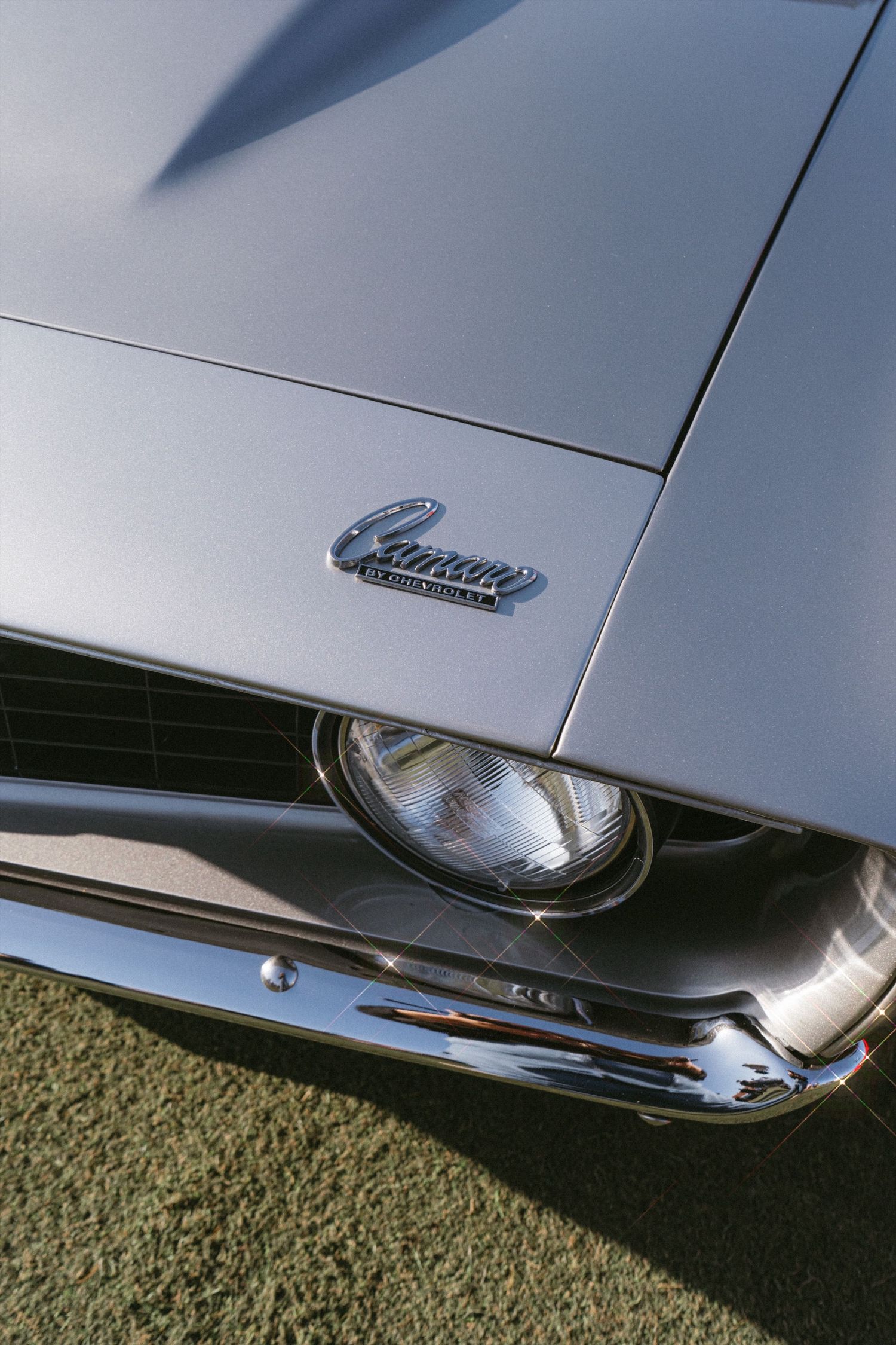 Close-up of classic Camaro headlight and chrome trim against silver bodywork.