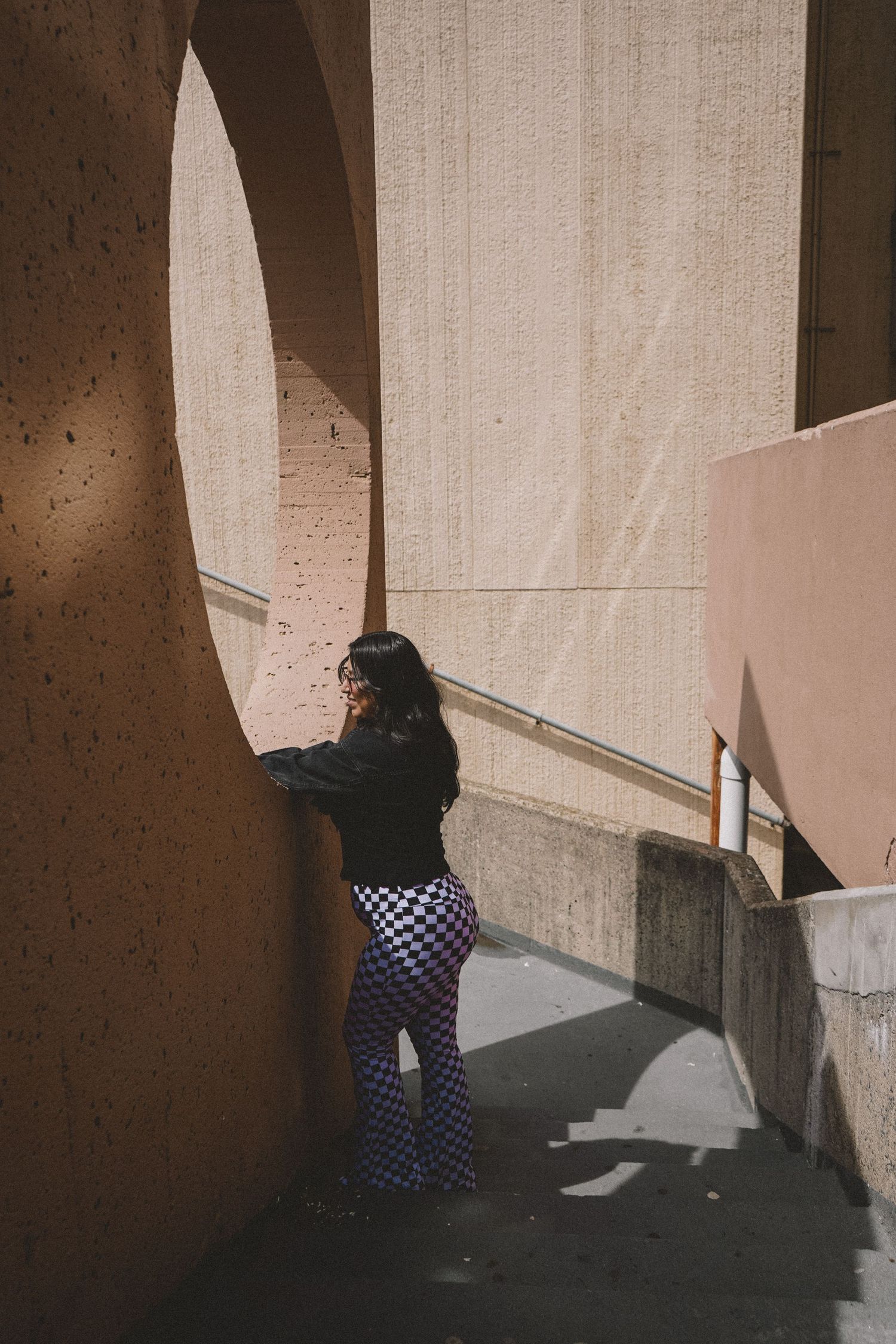Artistic shot of person in checkered pants leaning against sunlit concrete wall.