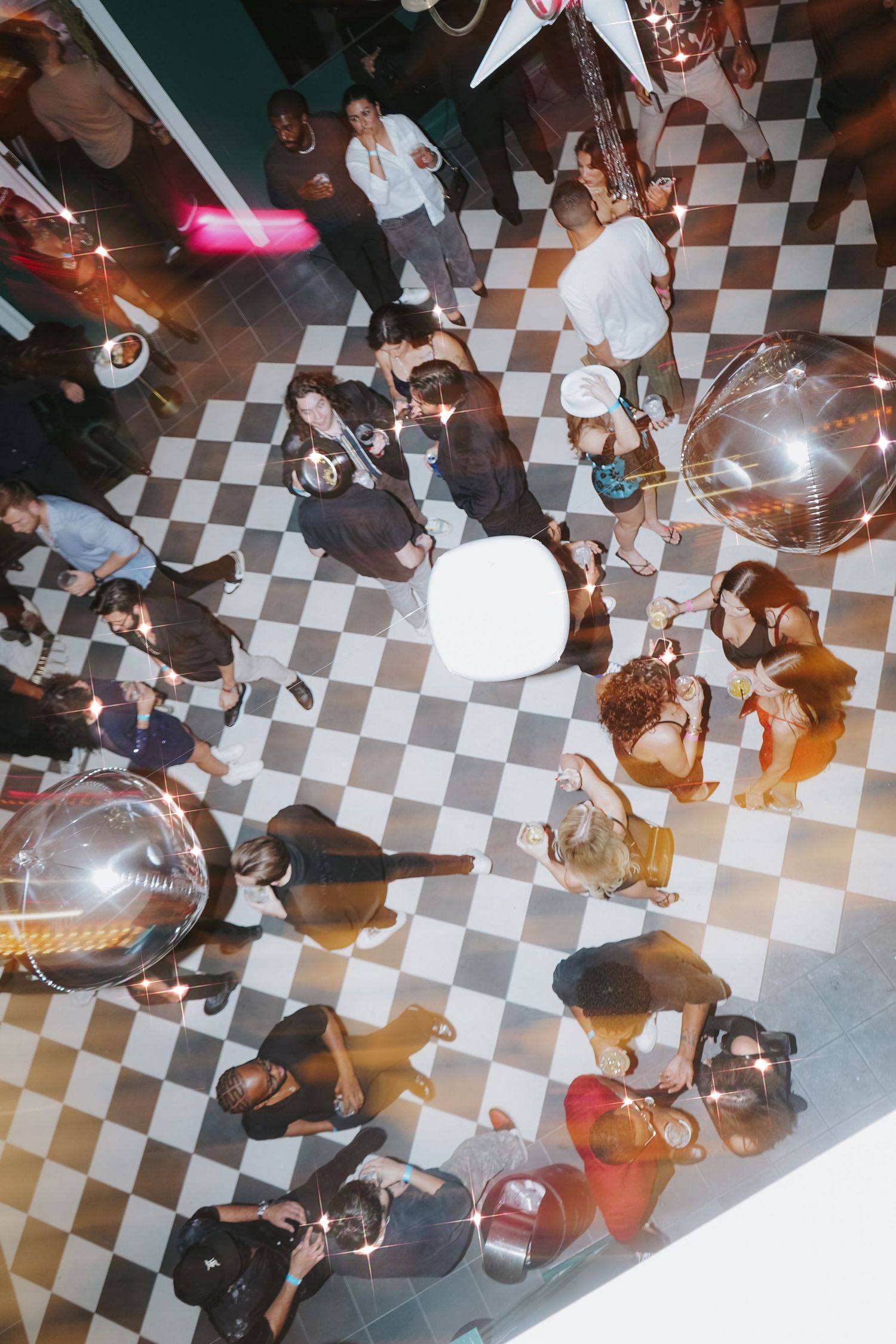 Aerial view of people dancing on a black and white checkered floor under disco balls.