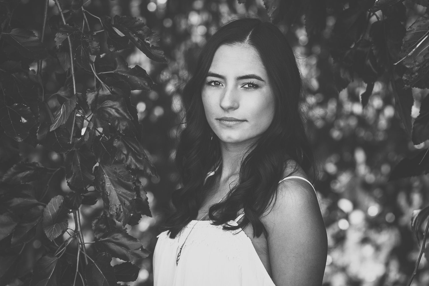 Black and white portrait of woman in white dress standing among foliage.