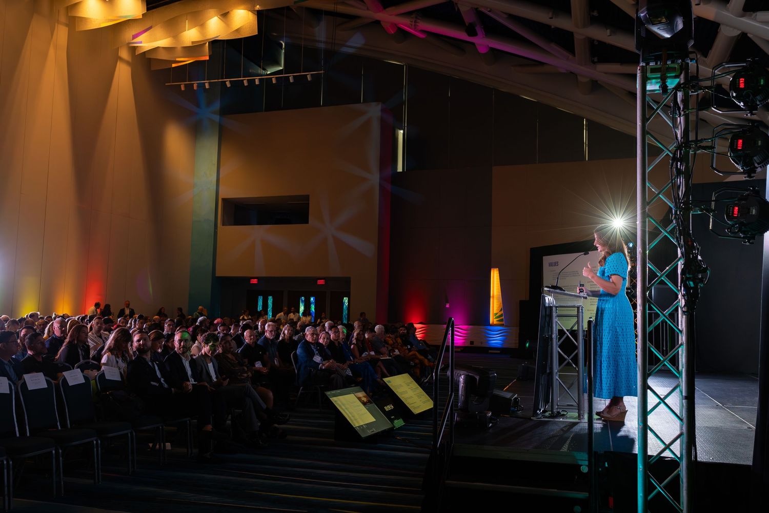 Dark event venue with dramatic lighting and stage setup showing multiple trusses and spotlights.