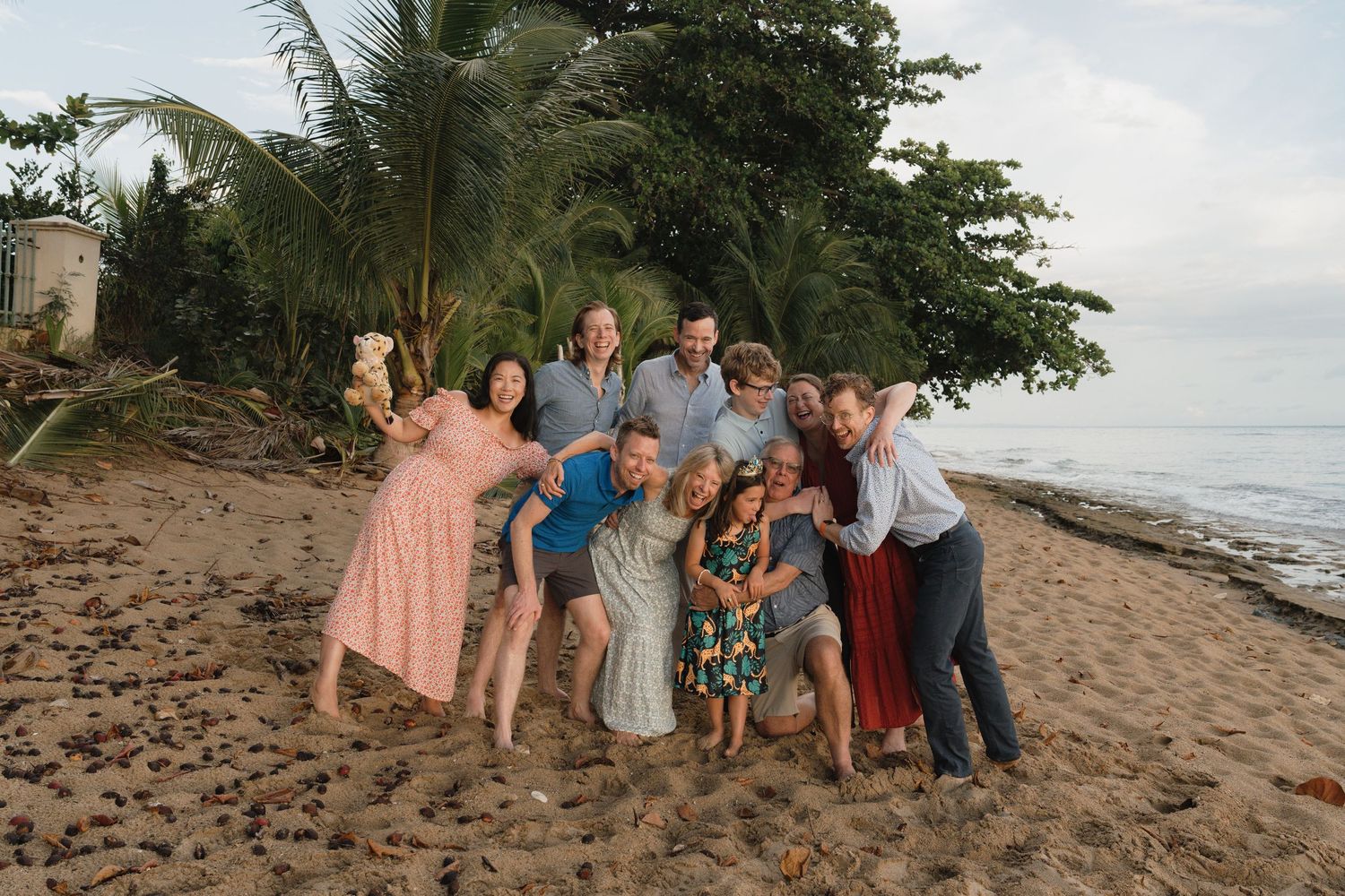 A joyful group of people posing together on a tropical beach with palm trees and ocean in the background.