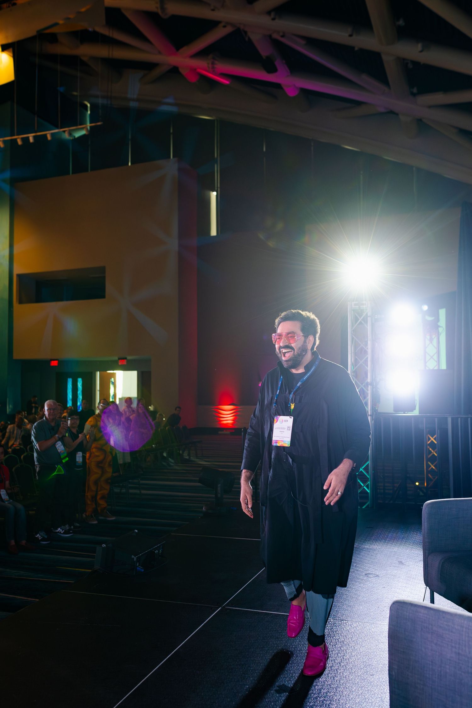 Speaker on stage at an event with dramatic lighting and audience in background.
