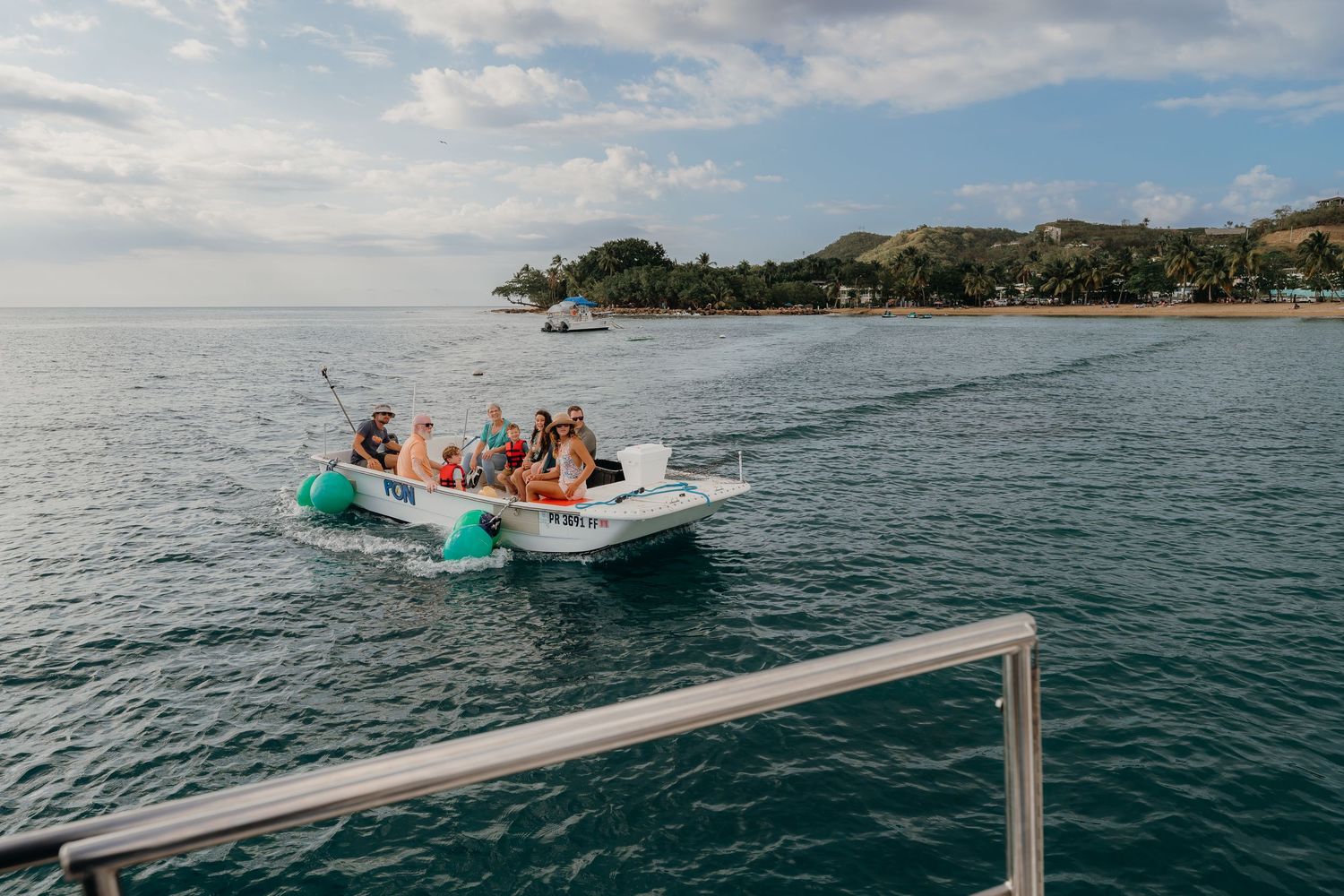 Group of tourists enjoying a boat ride on calm turquoise waters near a tropical island coastline on a sunny day.