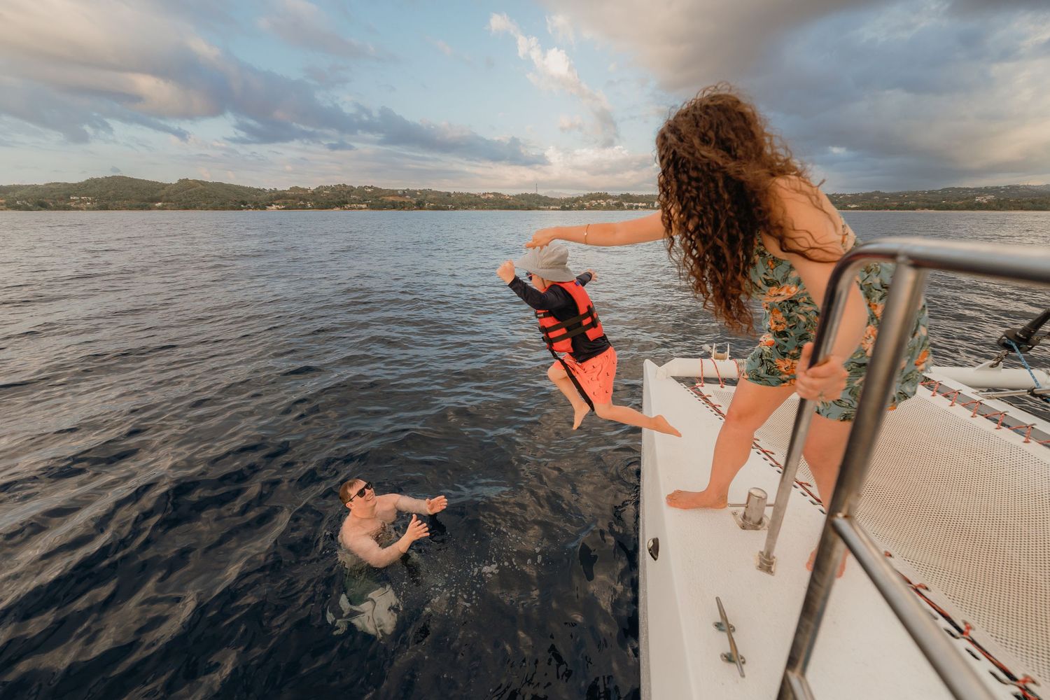 Person jumping off yacht into ocean water while woman watches from boat deck and swimmer enjoys the sea.