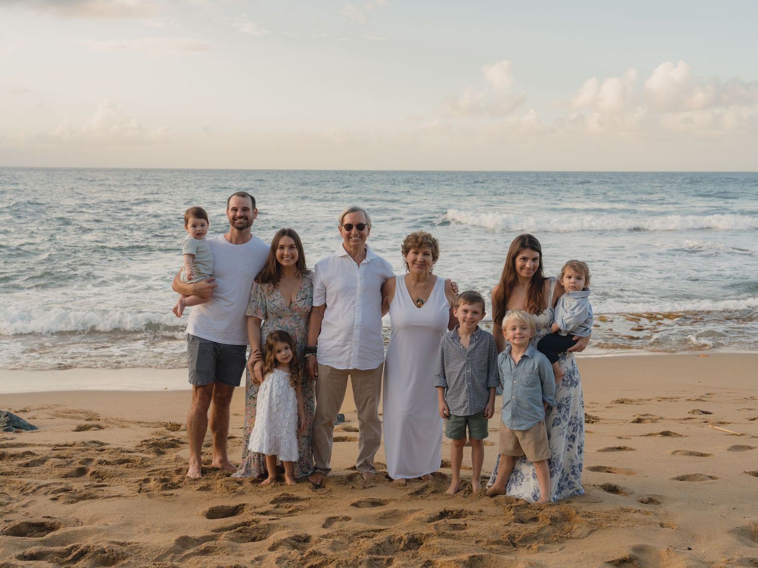 Large family group portrait on a sandy beach at sunset with ocean waves in the background.
