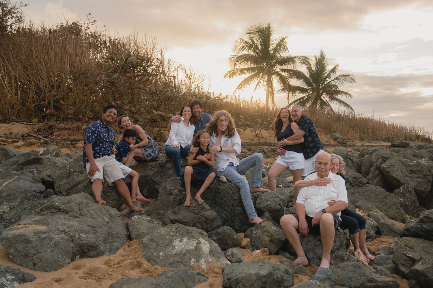 Family group portrait on rocky beach at golden sunset with palm tree, casual coastal photography session in Hawaii.