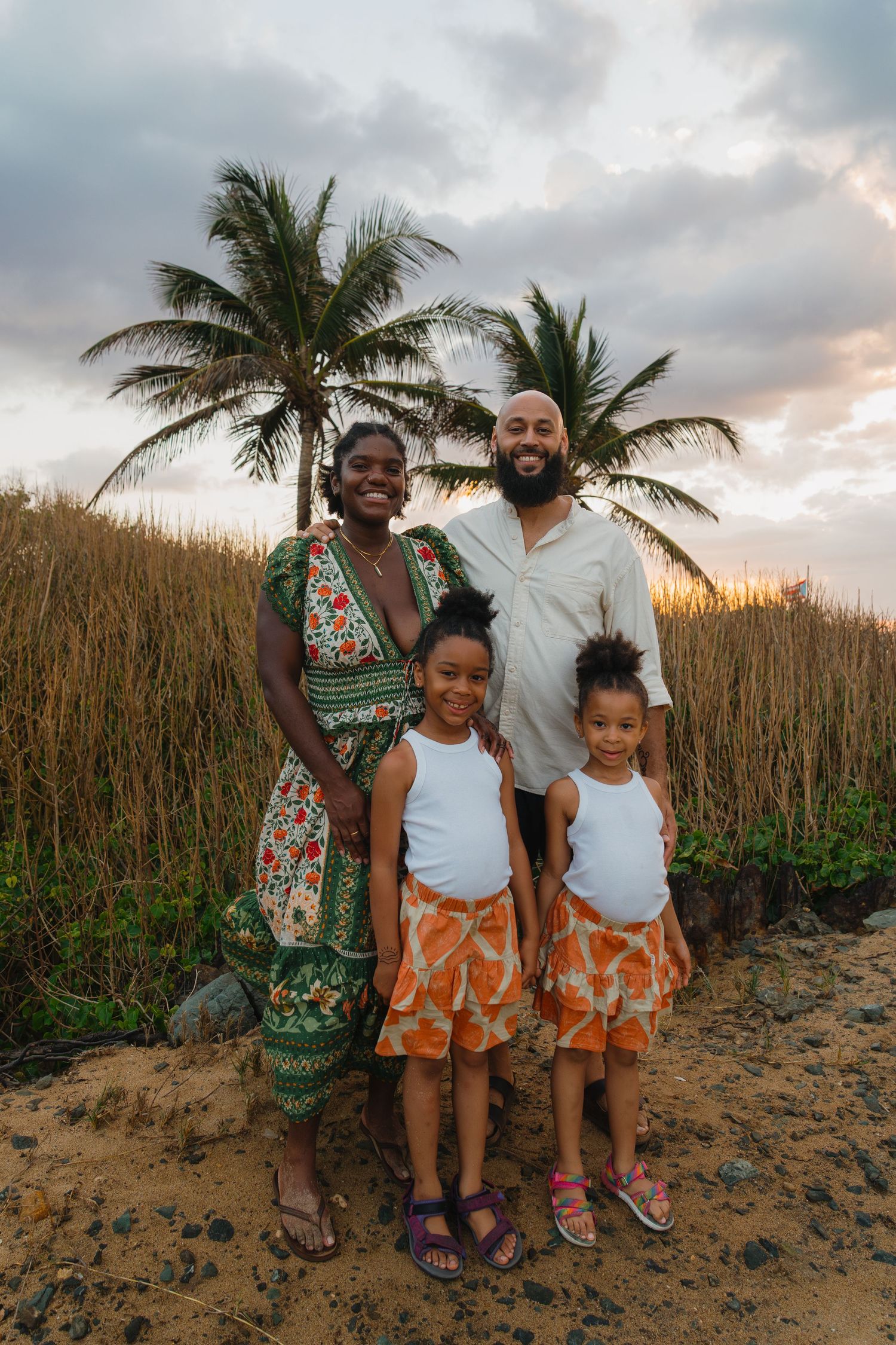 Family portrait on a beach with palm trees at sunset.