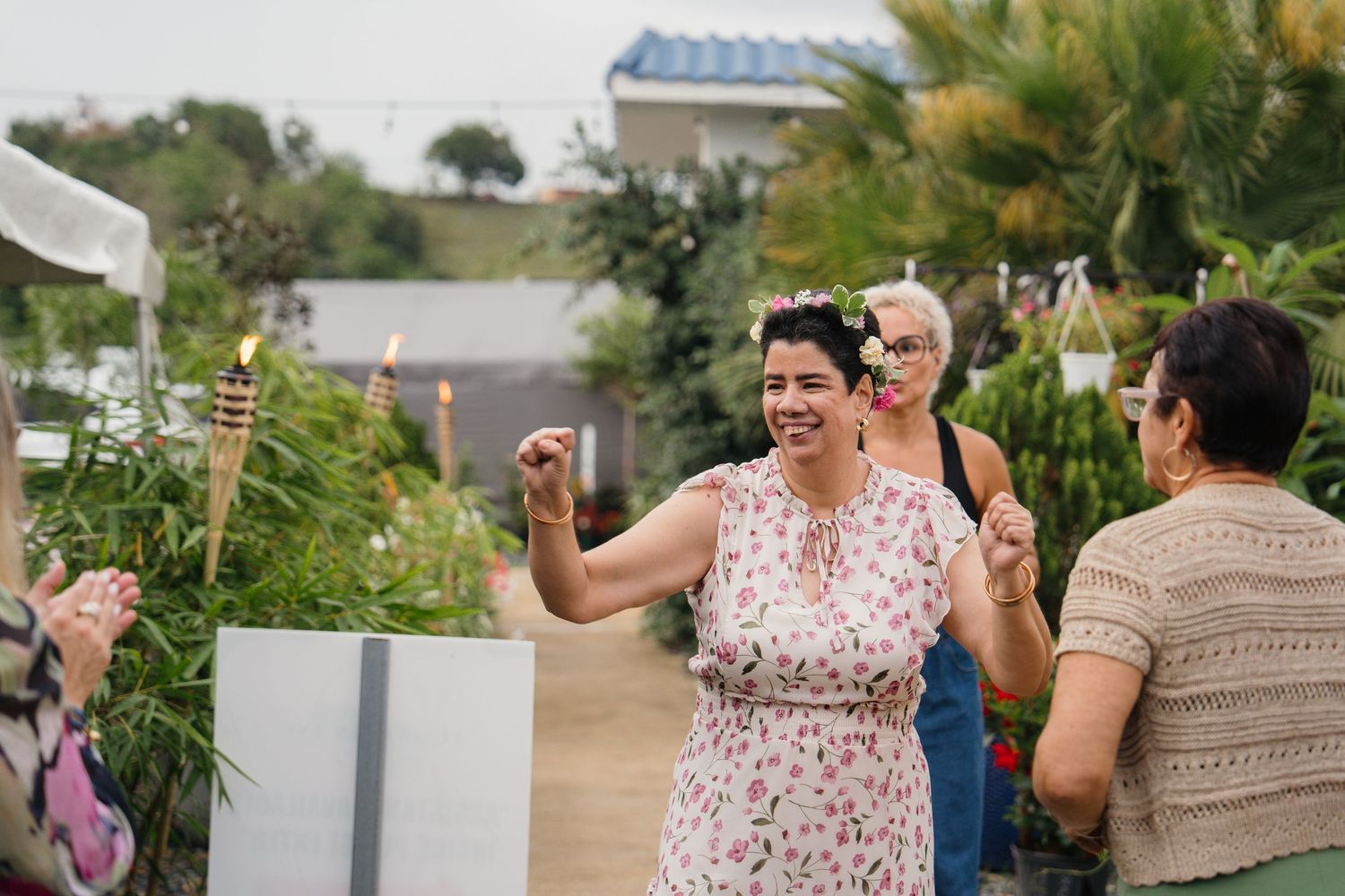 Woman in floral dress celebrating outdoors at a garden party with tiki torches and greenery.