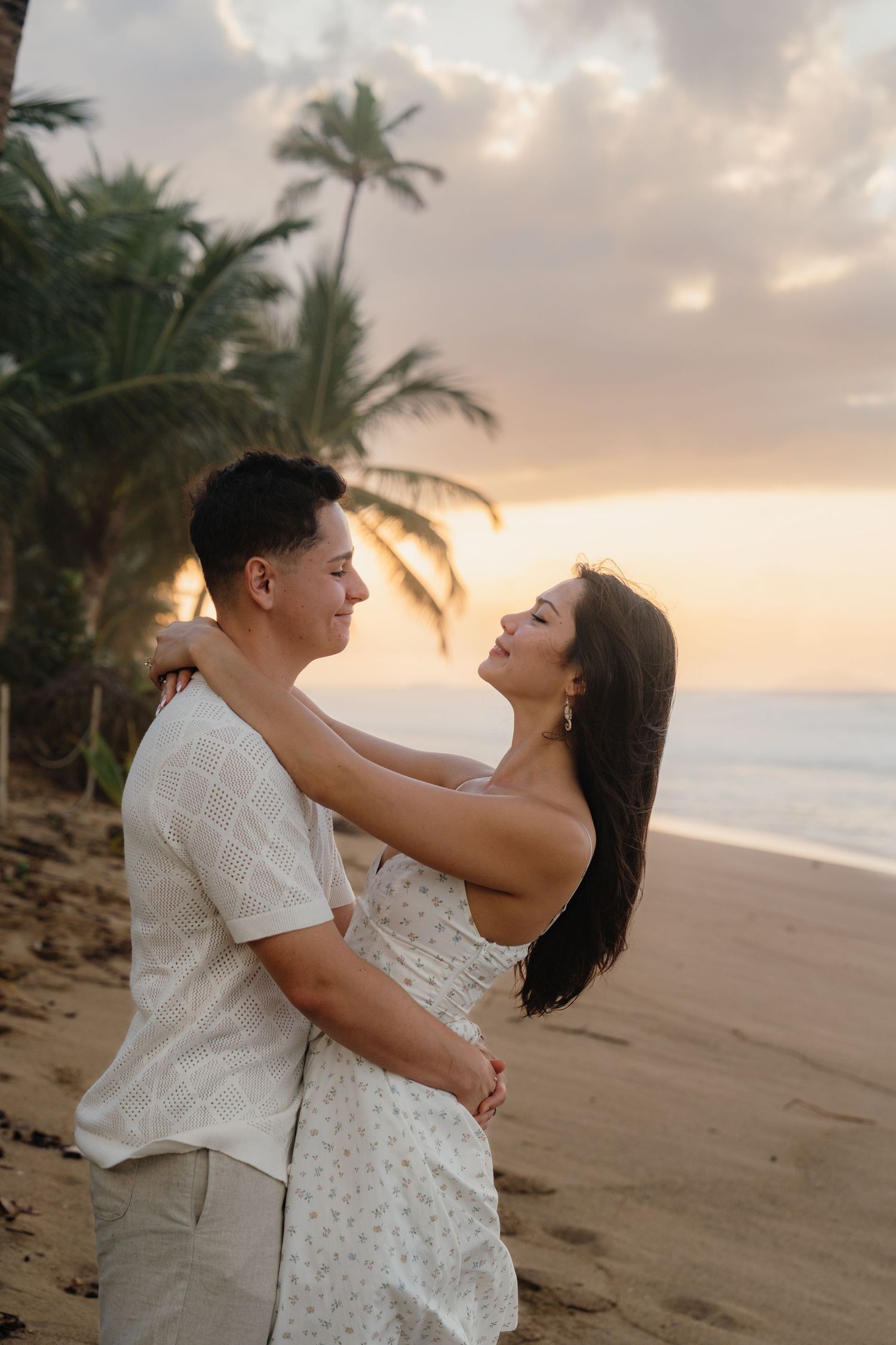 Couple embracing on a tropical beach at sunset with palm trees and ocean in the background.