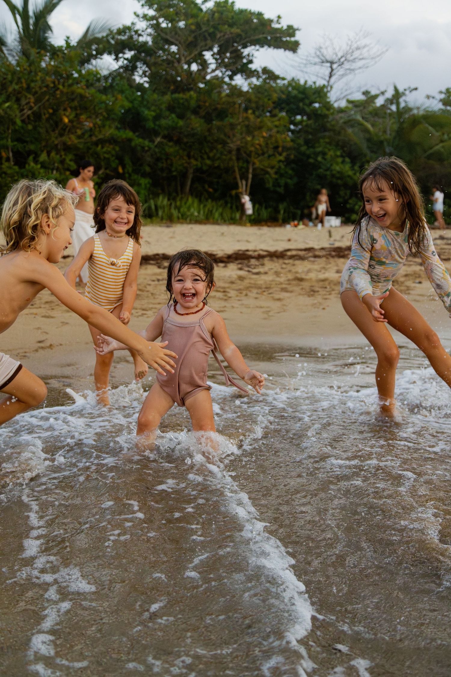 Friends splashing and playing in ocean waves at the beach during sunset.