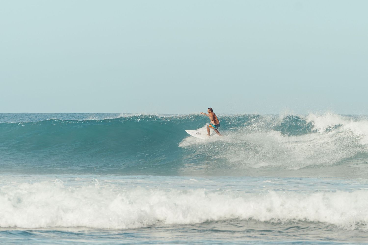A surfer rides a wave on a white surfboard in the ocean on a clear day.
