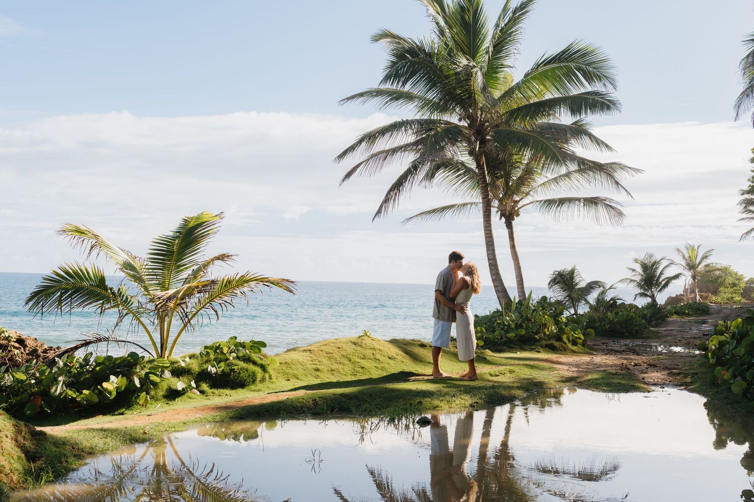 Couple embracing near a tropical pool with palm trees and ocean views at a luxury resort.