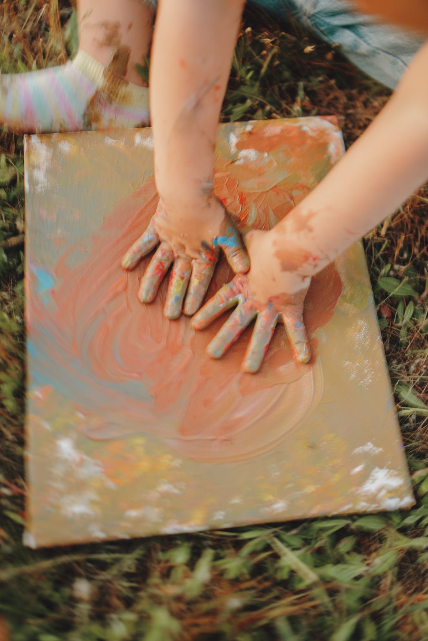 Small hands making colorful paint art on a canvas outdoors.
