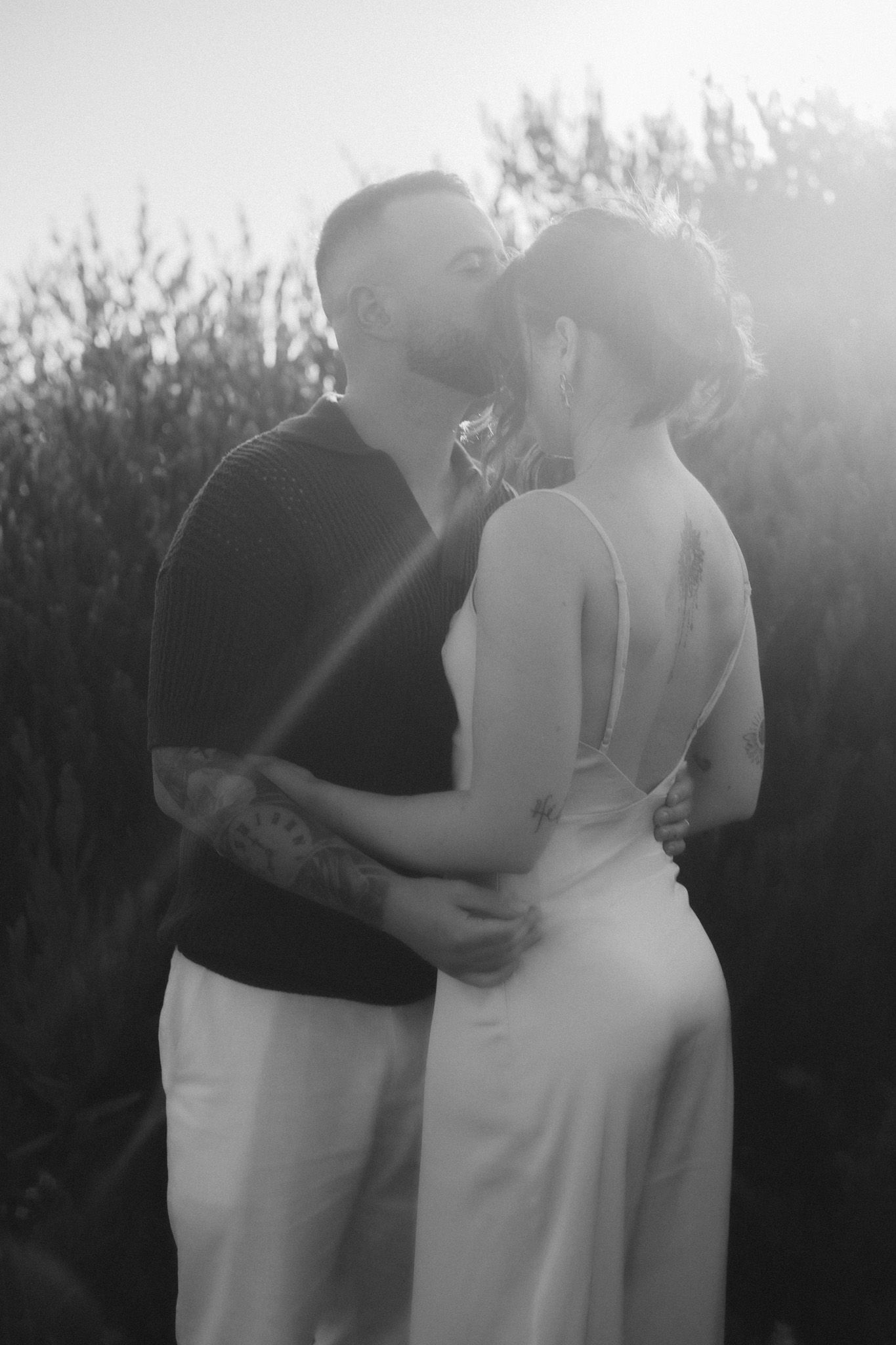 Silhouetted figures embracing at sunset with natural foliage in the background.