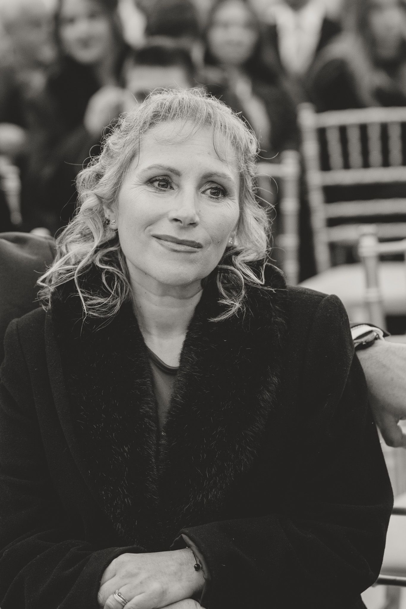 Guest in black attire watches wedding ceremony with an emotional expression.