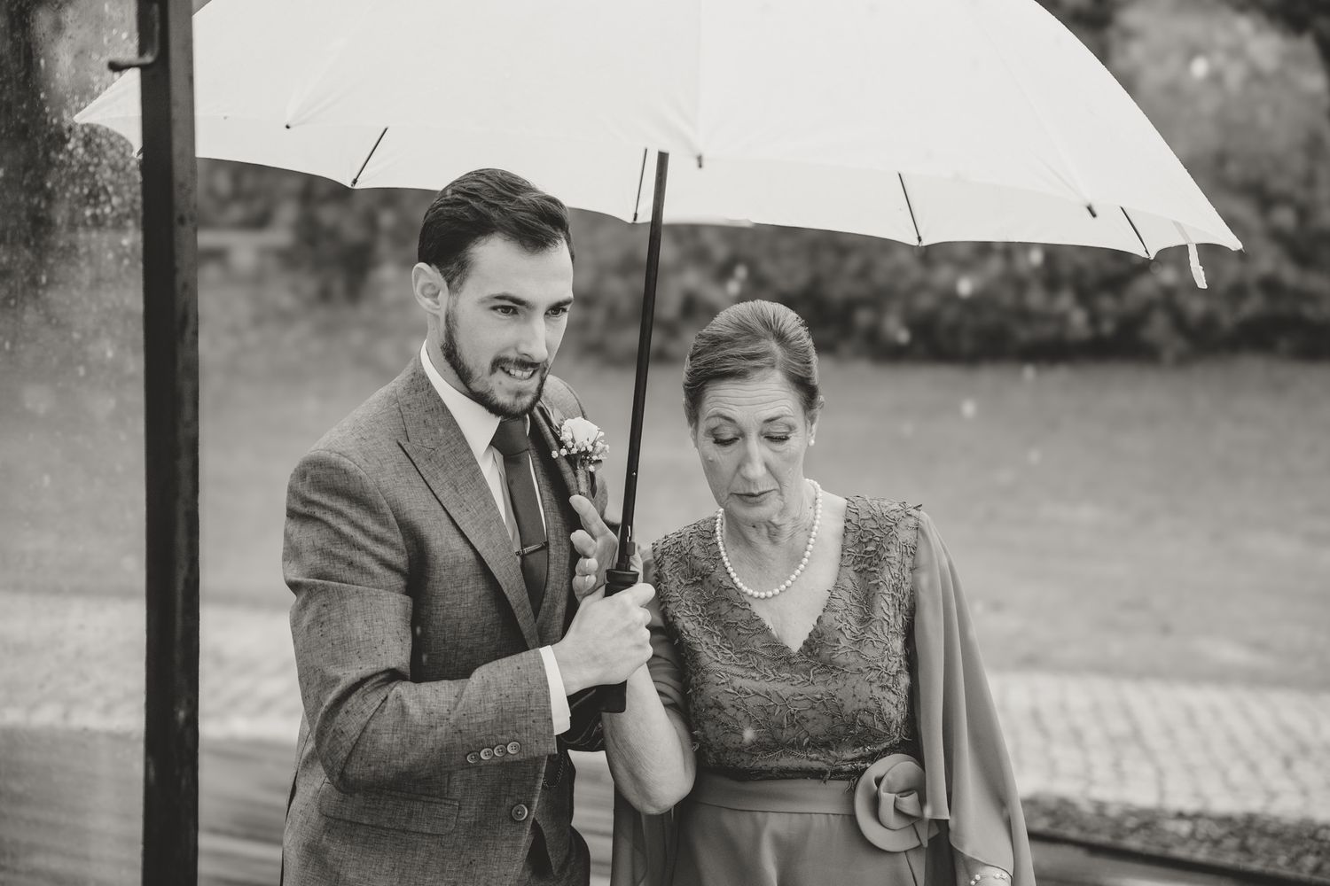 Black and white photo of couple sharing an umbrella outdoors.