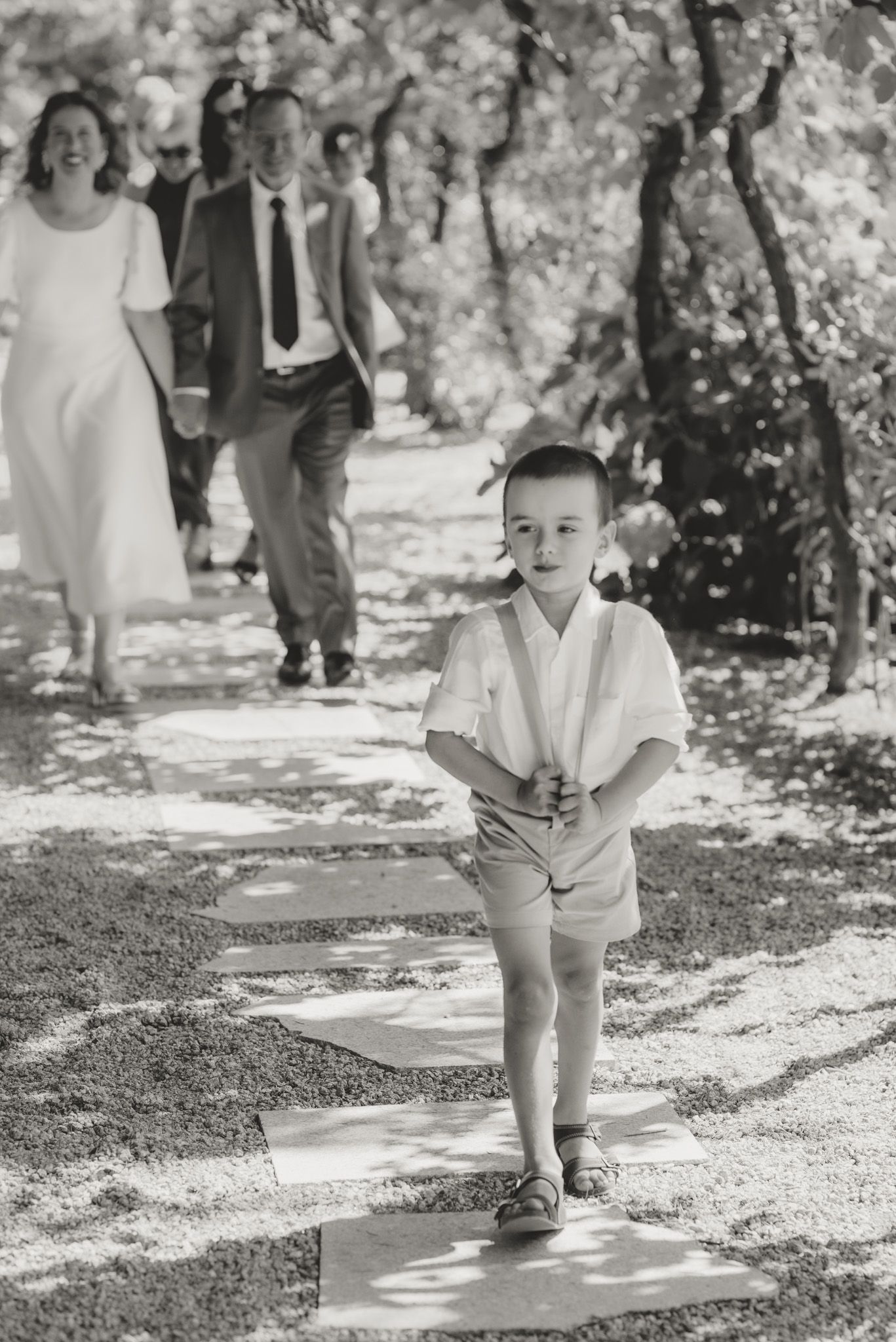 Black and white photo of small child walking on garden pathway.
