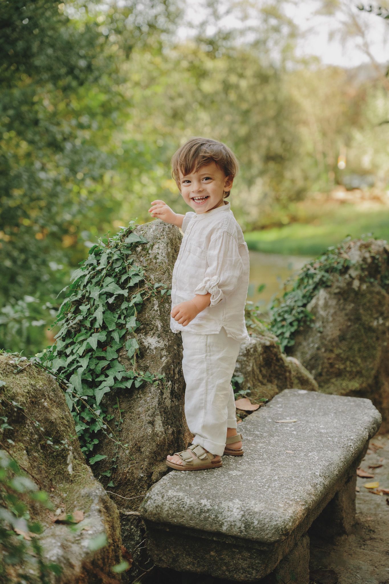 Small child in white outfit plays on stone steps in garden setting.