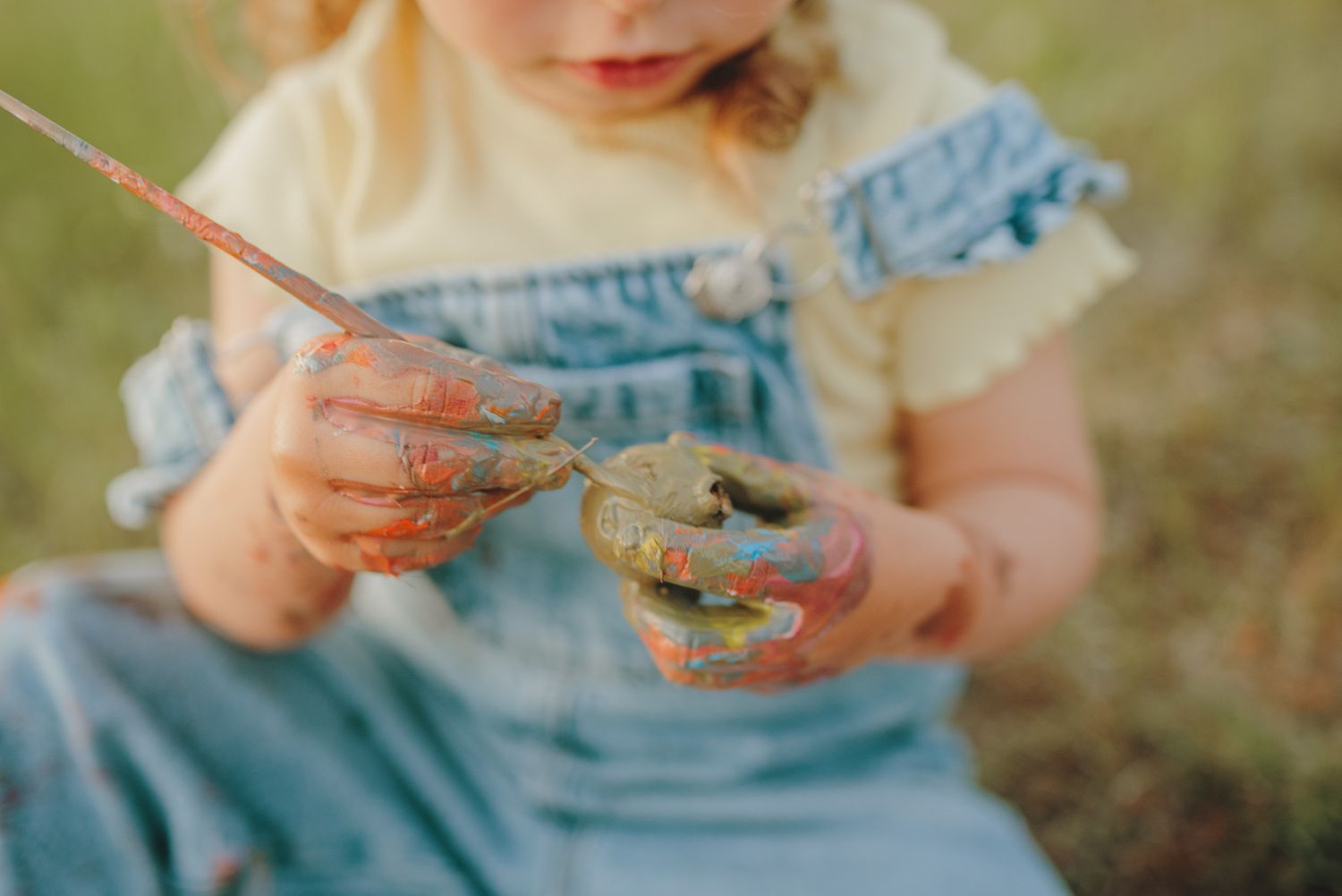Close-up view of hands holding a book while wearing denim overalls in a field.