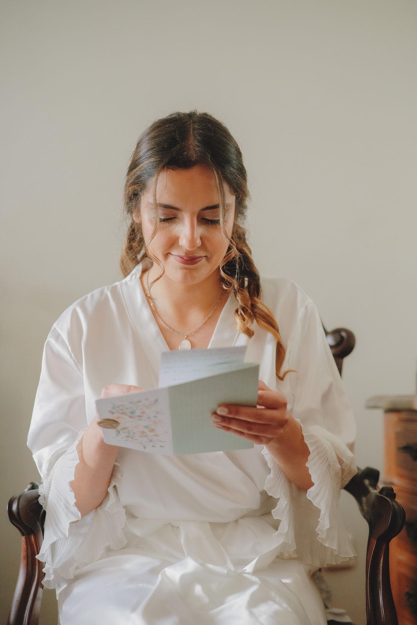 Person in white robe reading handwritten note during wedding preparations.
