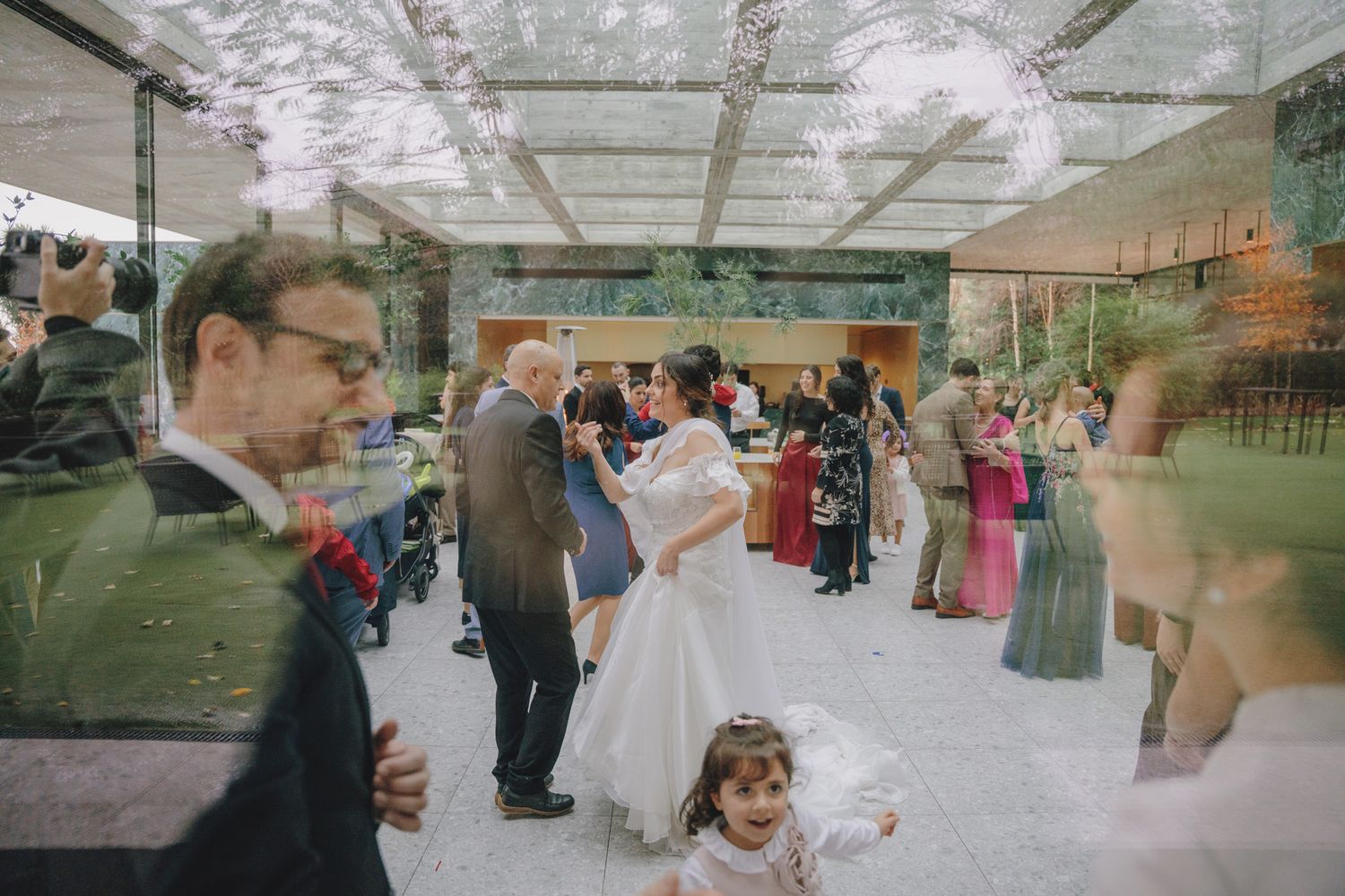 Wedding celebration captured under glass ceiling with natural lighting.