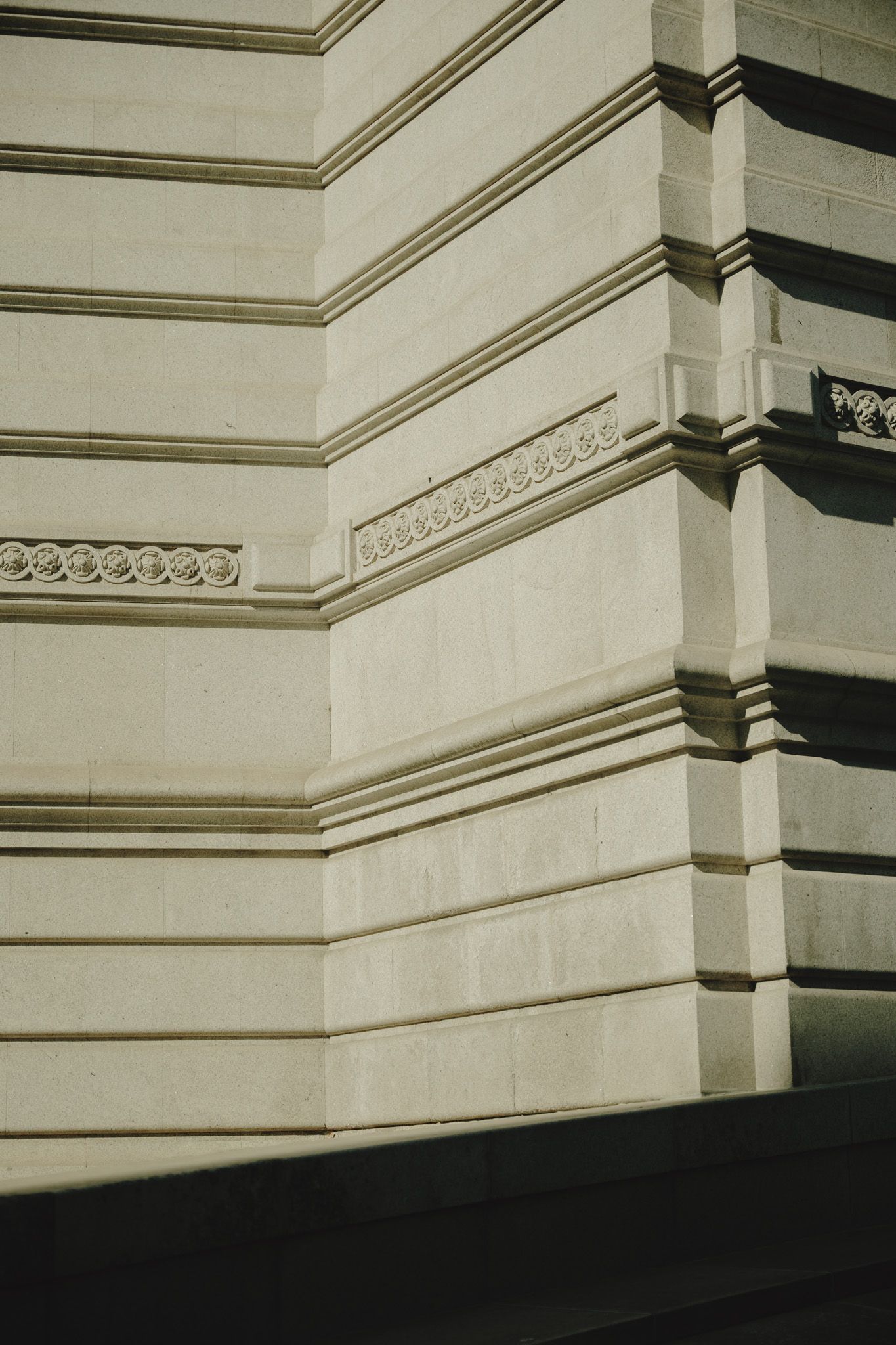 Architectural detail showing white stone walls with decorative moldings and shadows.