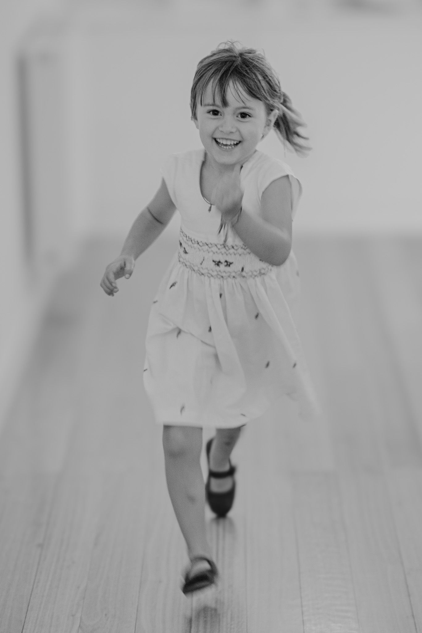 Black and white sequence of a young child running and playing on a wooden floor.