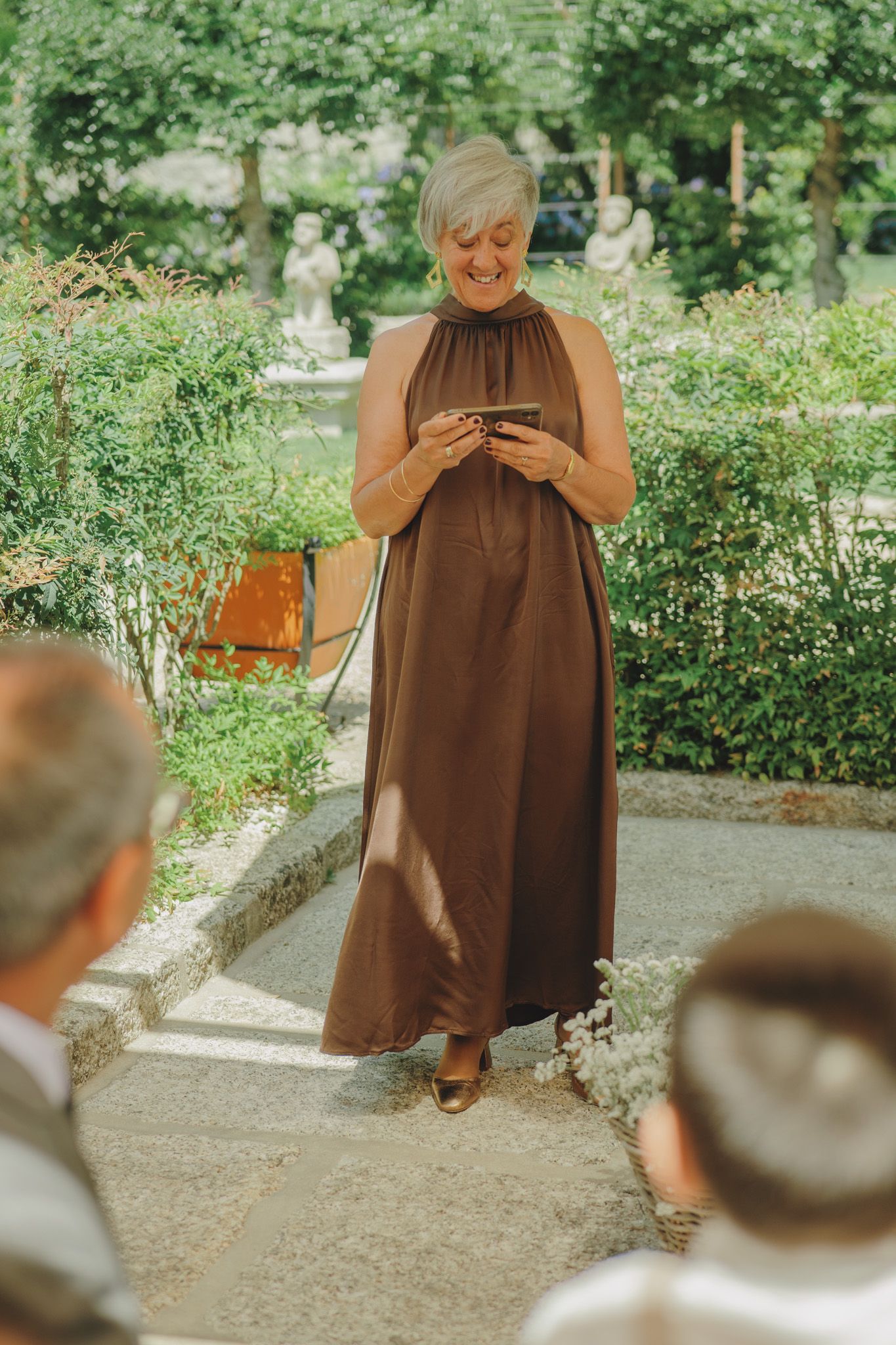 Person in brown dress stands on garden path during outdoor event.