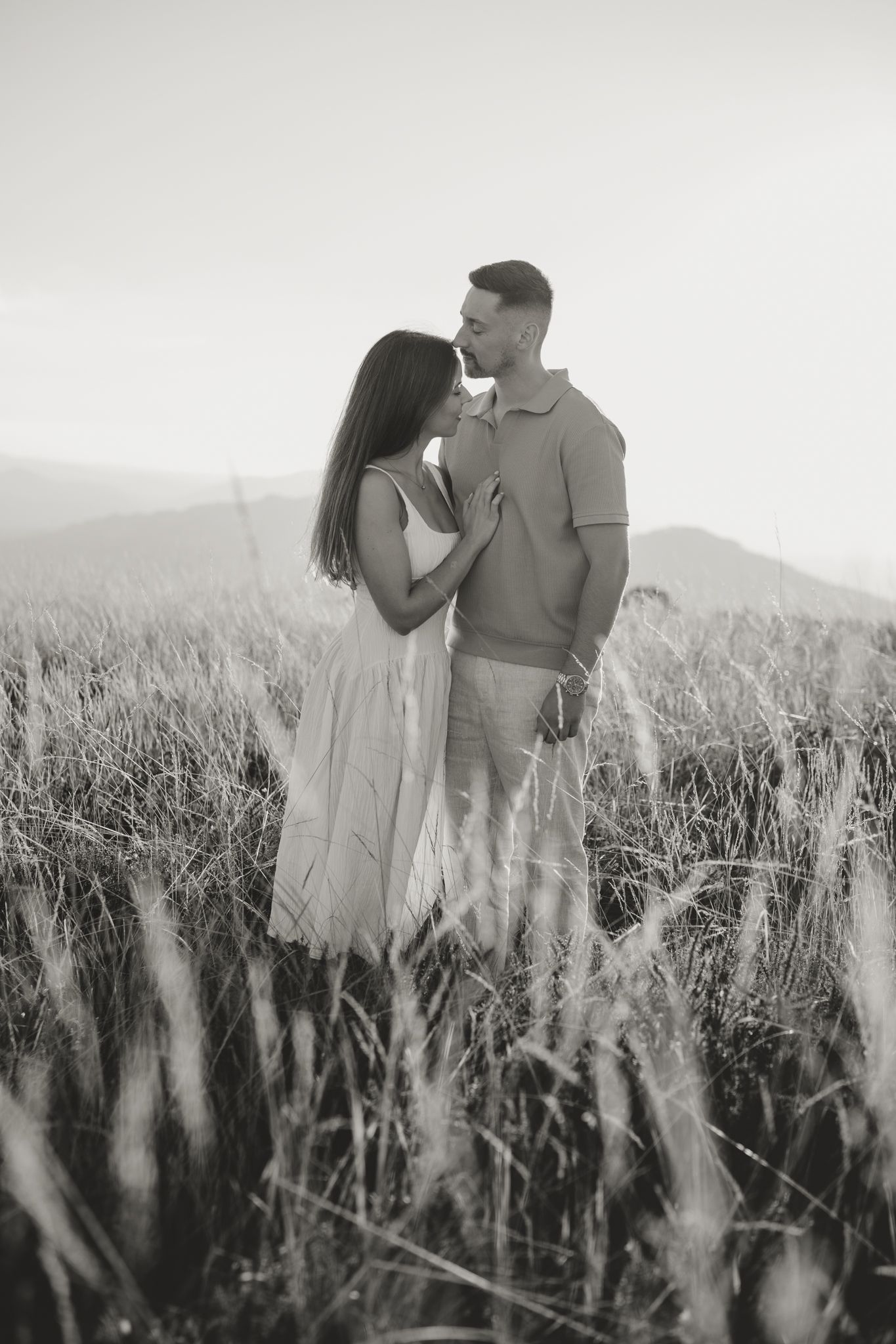 Black and white photo of a couple sharing an intimate moment in a field of tall grass.