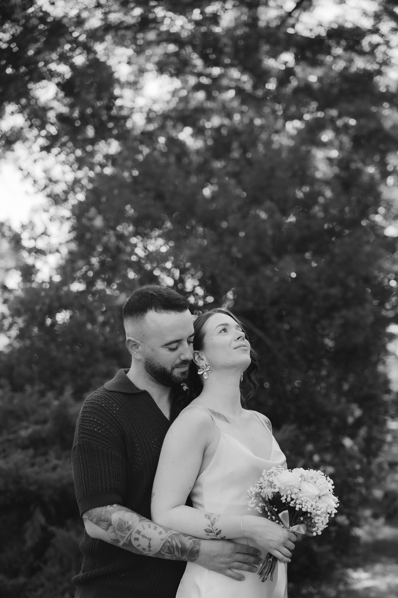 Intimate black and white portrait of couple embracing outdoors with white floral bouquet.