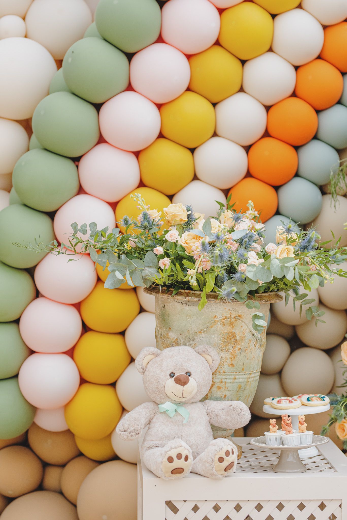 Pastel balloon wall with white lattice tables decorated with greenery and stuffed animals.
