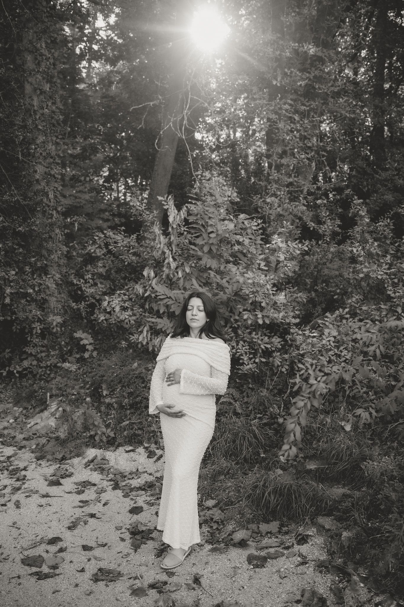 Black and white portrait of woman in white dress among trees.