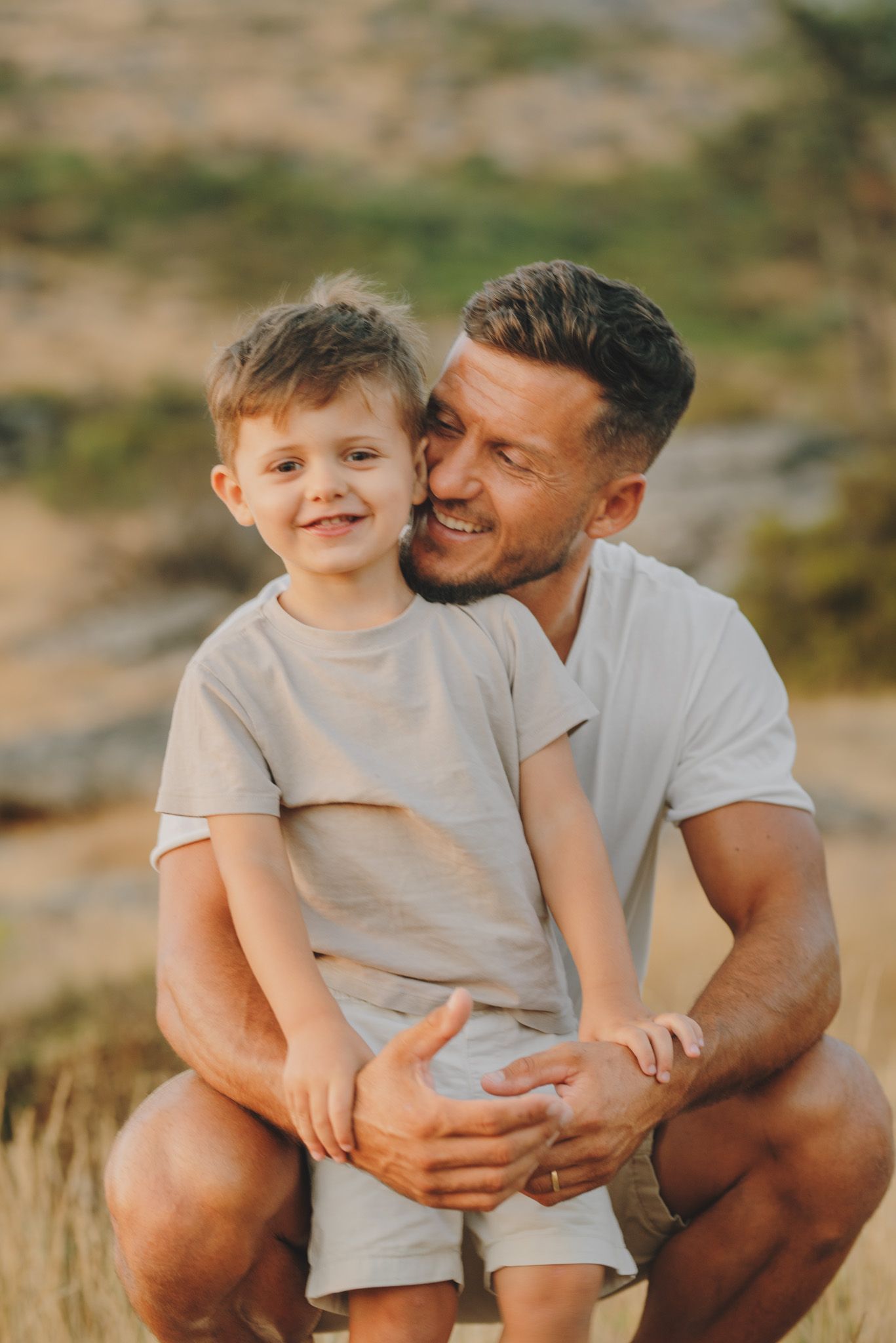 A heartwarming outdoor family moment captured in warm sunlight with natural scenery in the background.