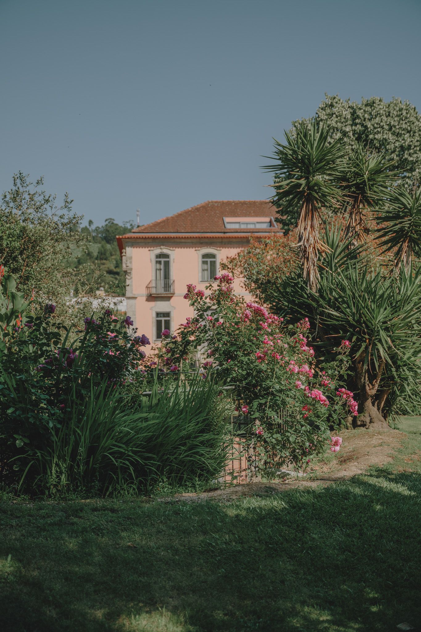 Mediterranean villa with pink walls surrounded by lush gardens and palm trees.