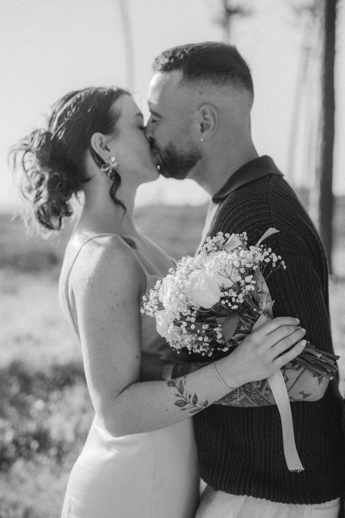Black and white portrait of couple sharing romantic kiss with bridal bouquet.
