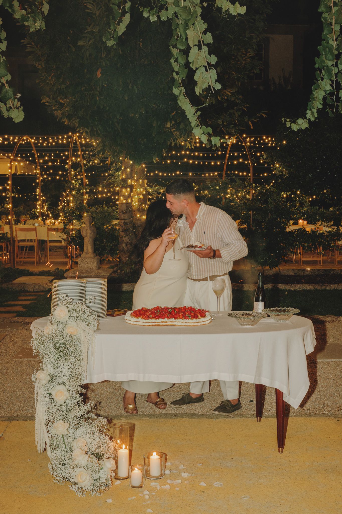 Outdoor evening reception table setup with string lights and floral decorations.