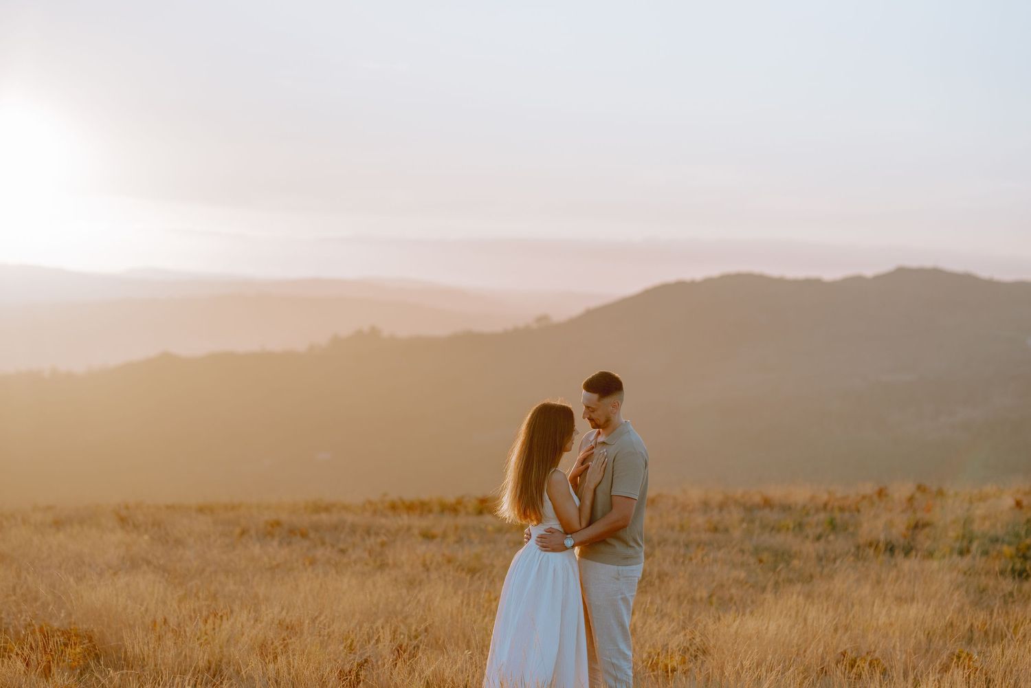 A couple in wedding attire stands together against a sunset mountain landscape.