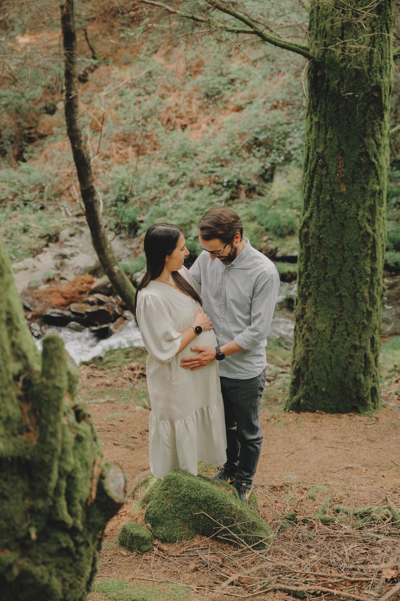 A couple shares tender moments together in a mossy forest setting.