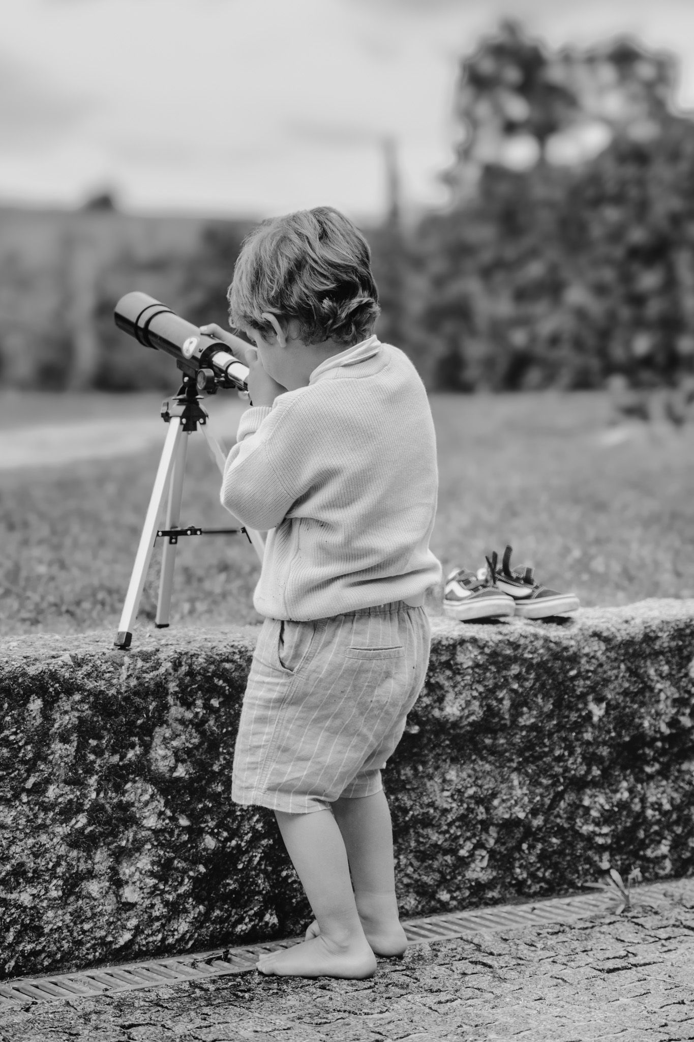 Black and white sequence of small child looking through telescope or binoculars outdoors.