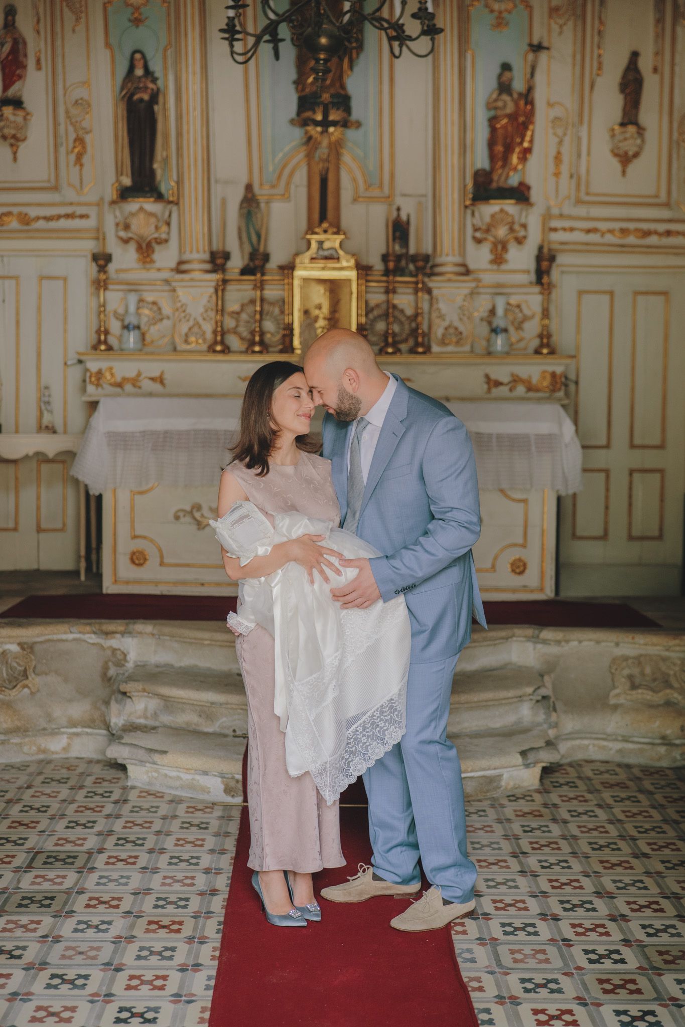 A baptism ceremony in an ornate church with decorative walls and patterned tile floors.