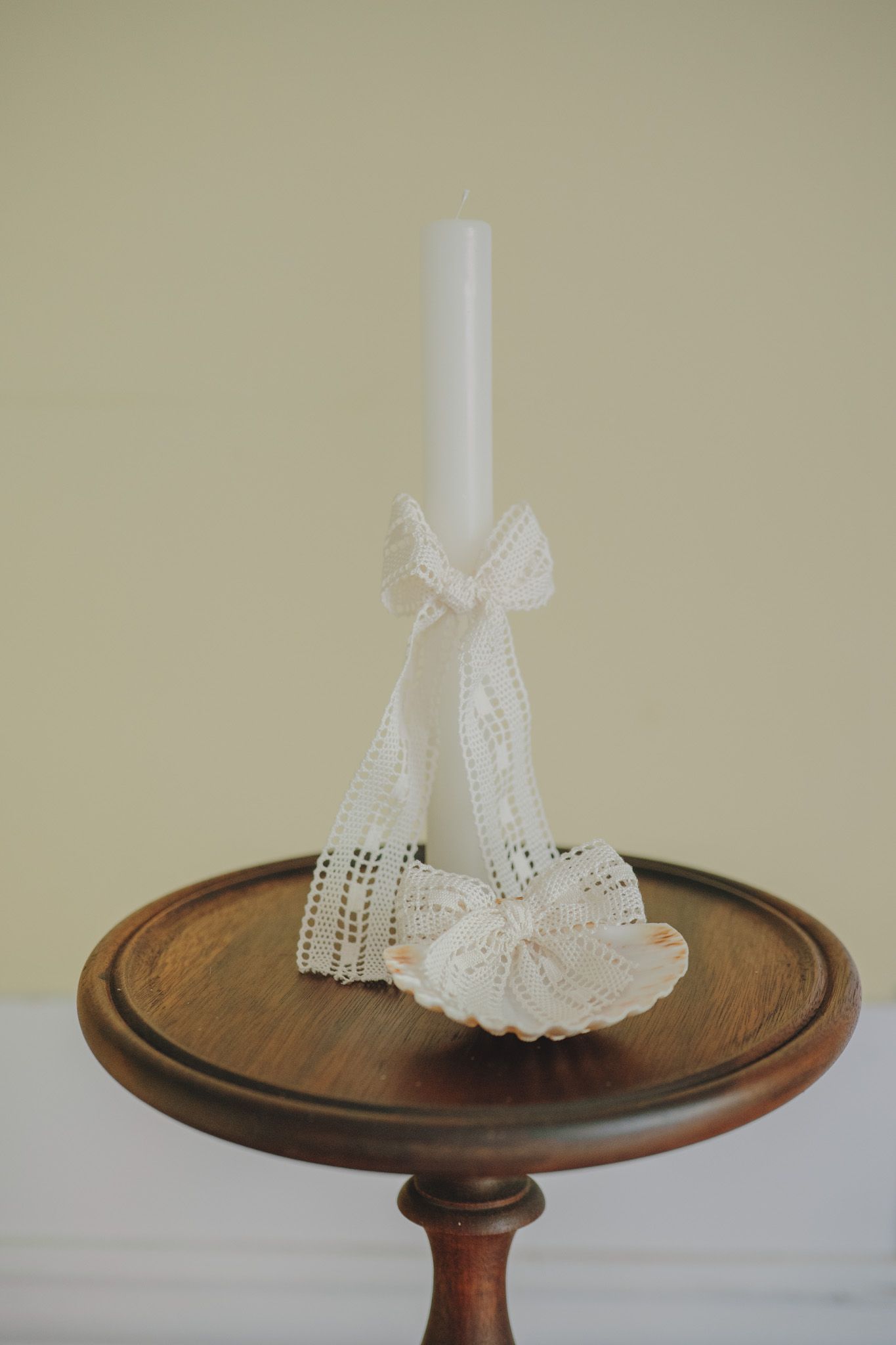 Delicate white lace bonnet displayed on a wooden pedestal table.